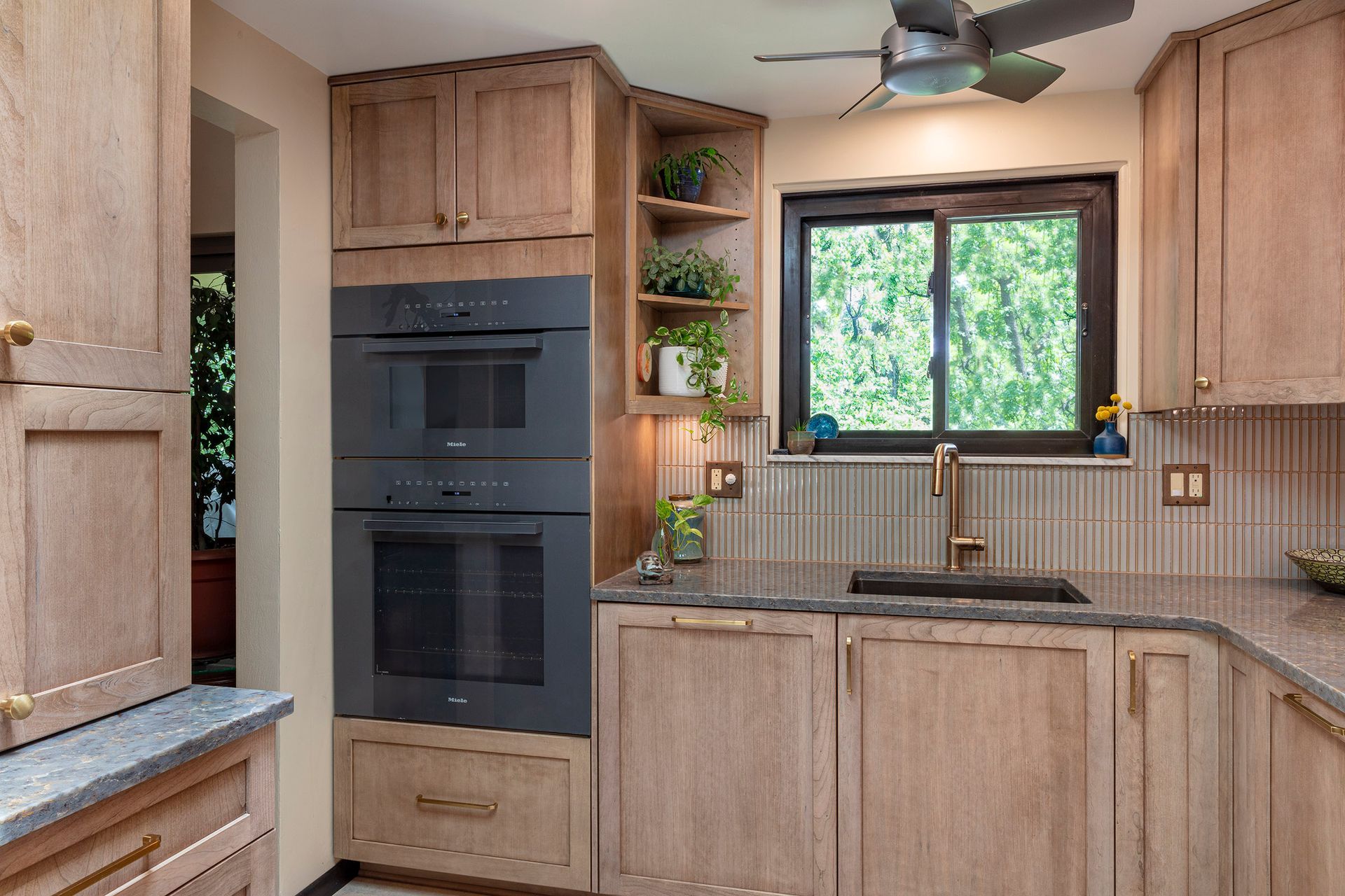 Wooden kitchen with built-in oven, sink under a window, and granite countertops