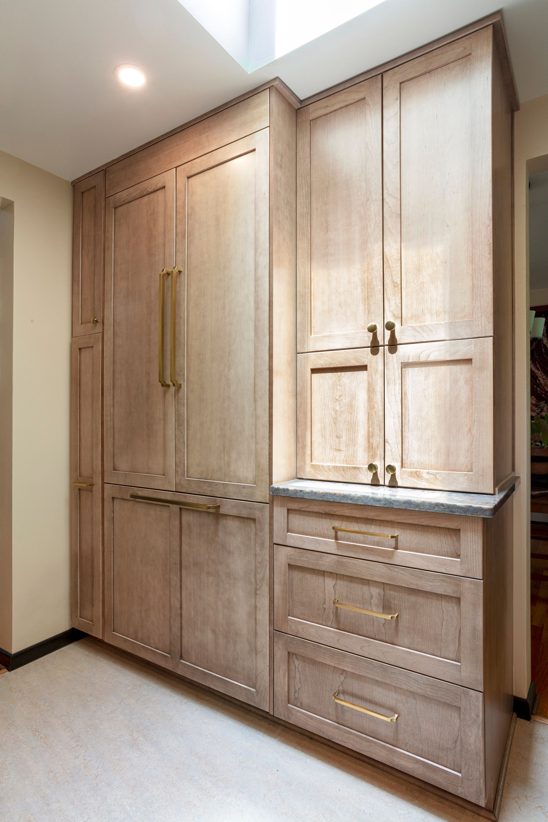 Built-in light wood cabinetry with gold handles and drawers in a hallway or kitchen nook