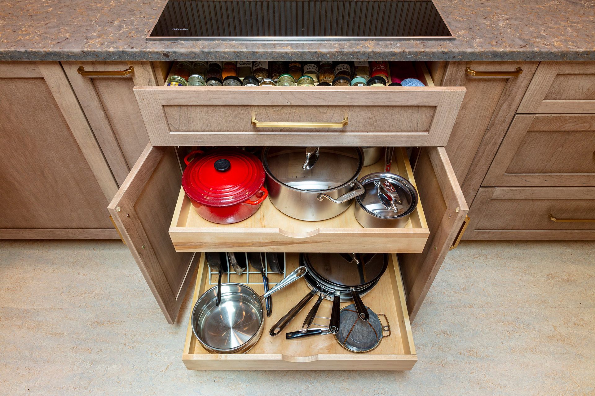 Kitchen cabinet with pull-out shelves holding red, silver, and black pots and pans