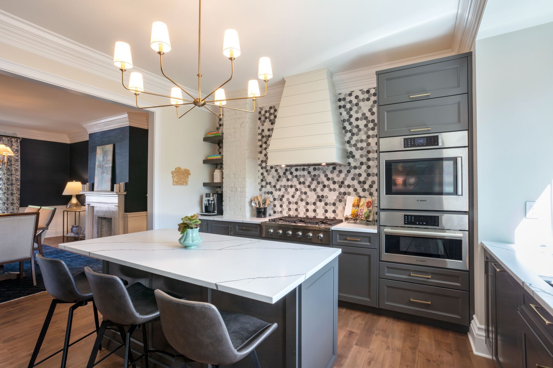 Modern kitchen with large island, gray cabinetry, patterned backsplash, and dining chairs under a chandelier.