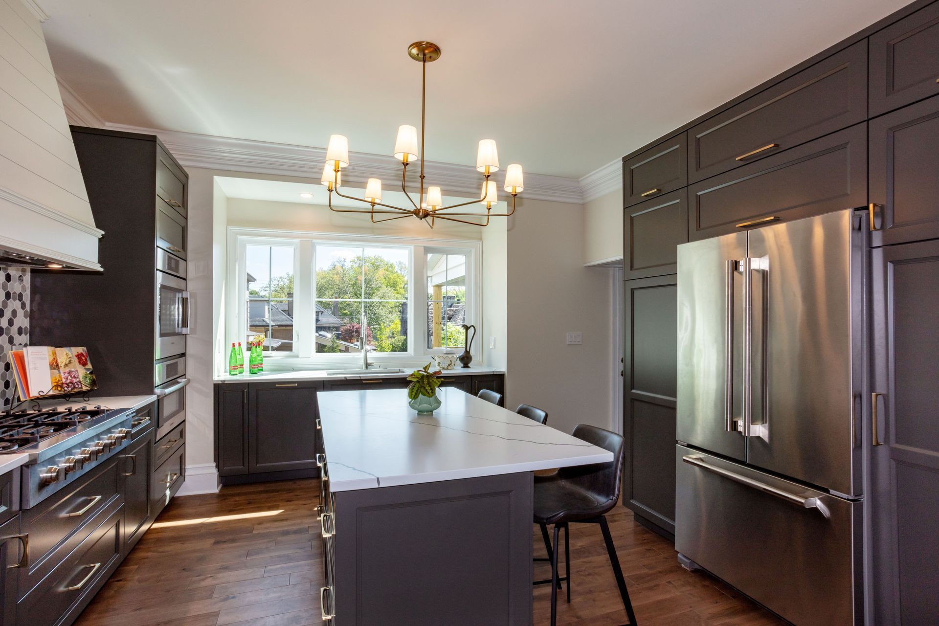 Modern kitchen with dark cabinets, stainless steel fridge, island, and bright window over the sink