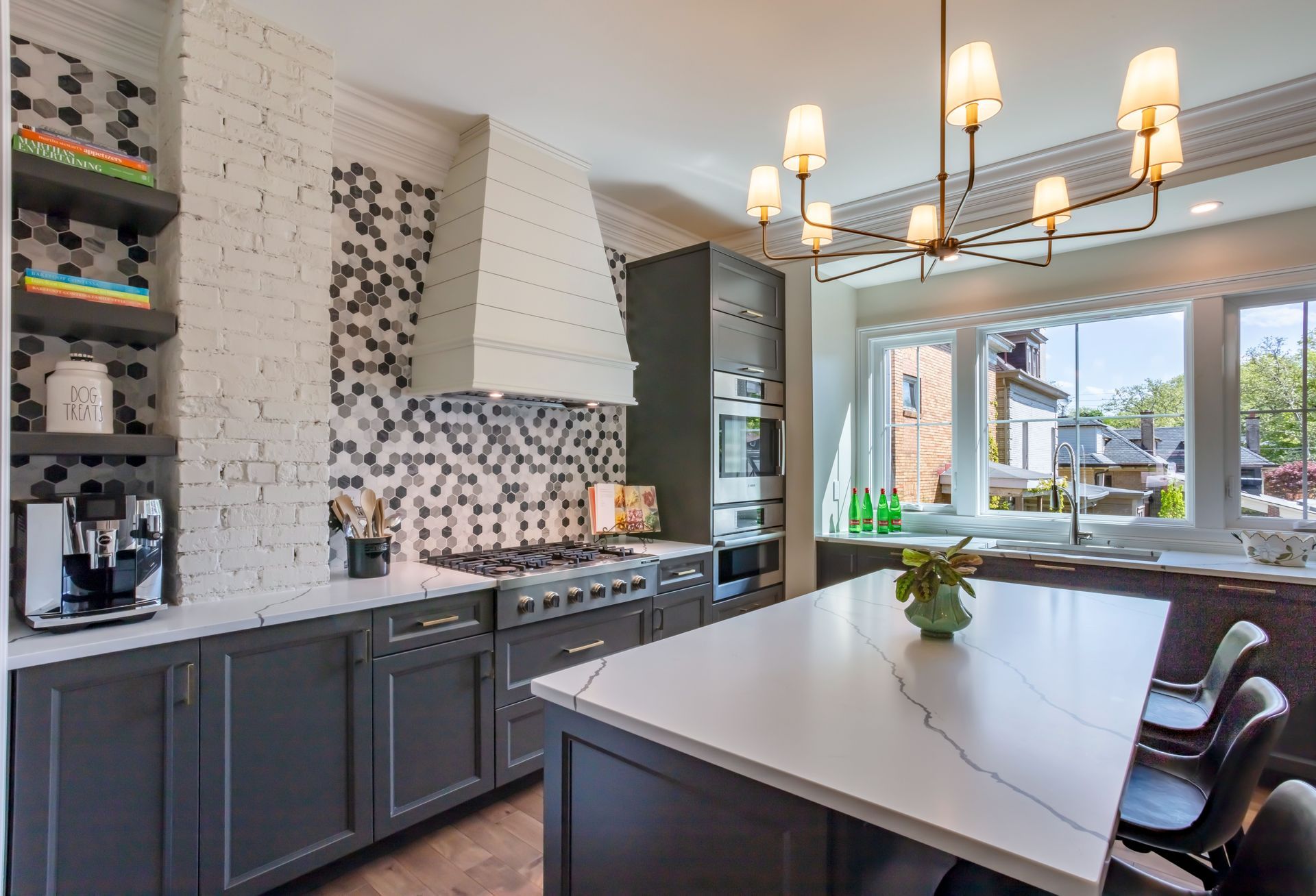Modern kitchen with dark cabinets, white tile backsplash, island, and large window under pendant lights