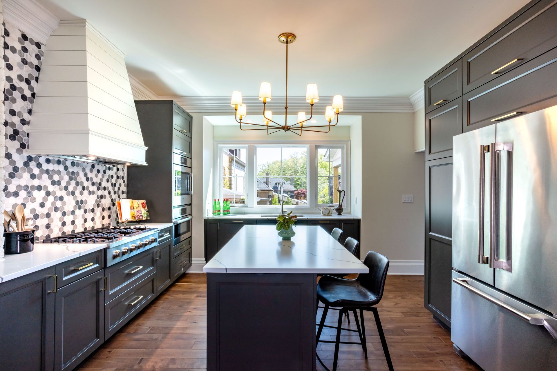 Modern kitchen with dark cabinets, stainless steel appliances, island, and a chandelier by a window