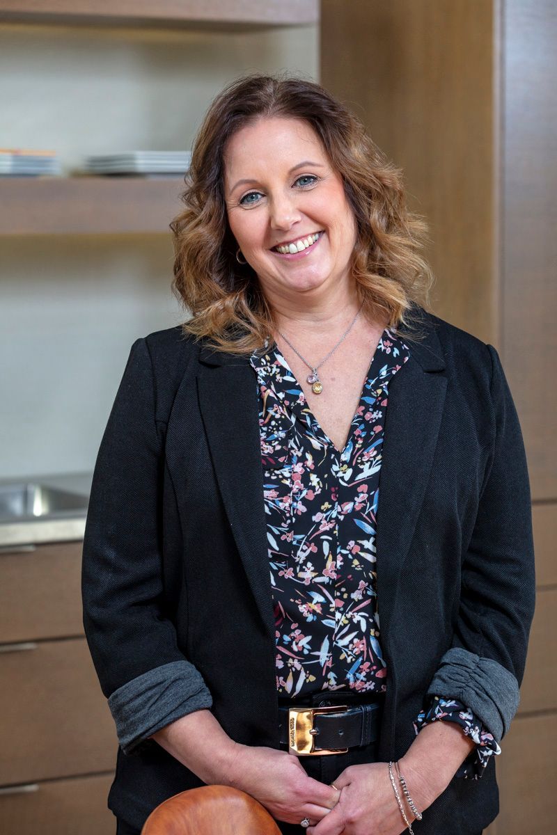 Smiling woman in a black blazer standing indoors against a modern office background