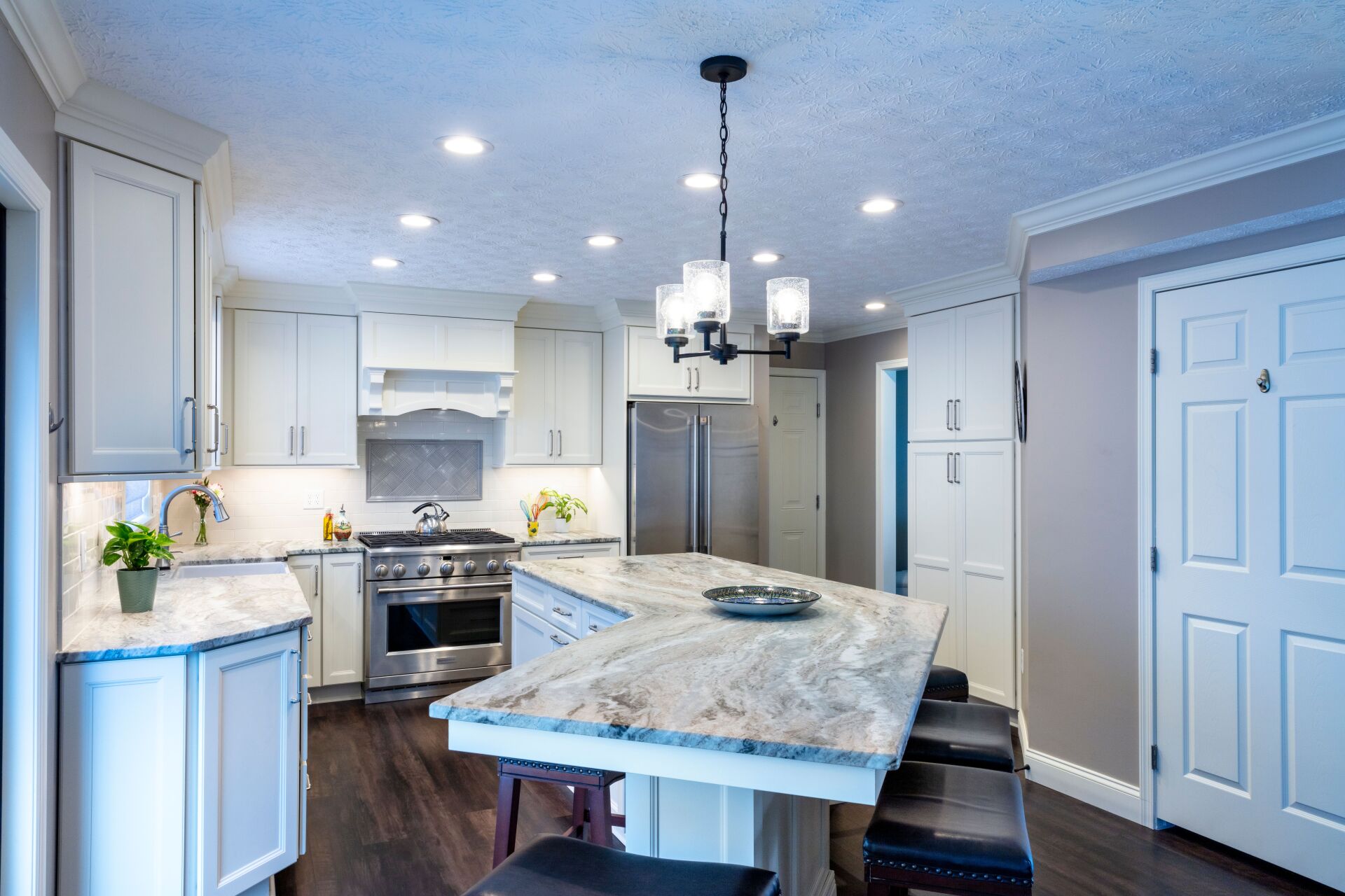 Bright modern kitchen with white cabinets, marble island, stainless stove, and pendant lights