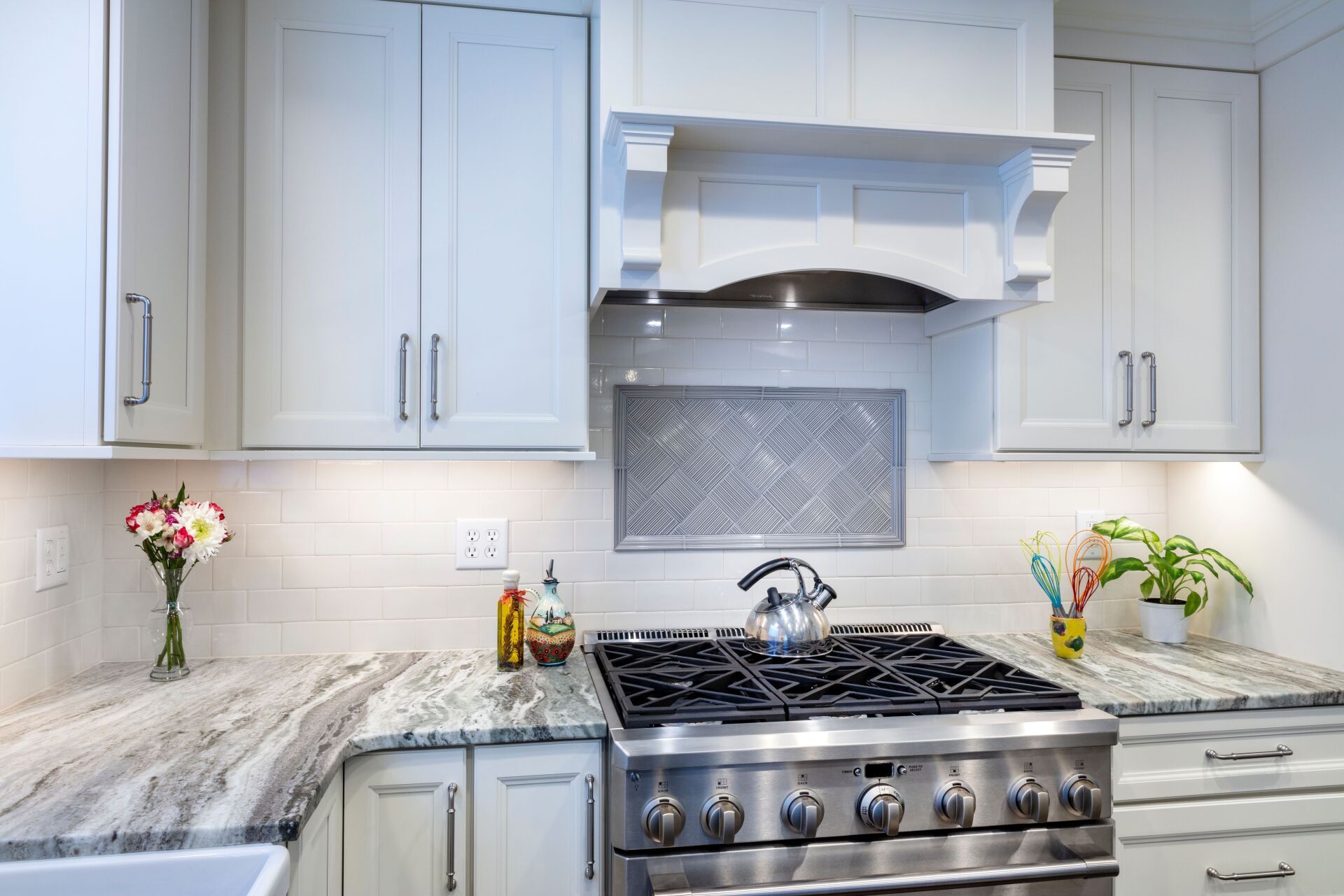Modern kitchen with white cabinets, marble counters, stainless steel stove, and decorative flowers