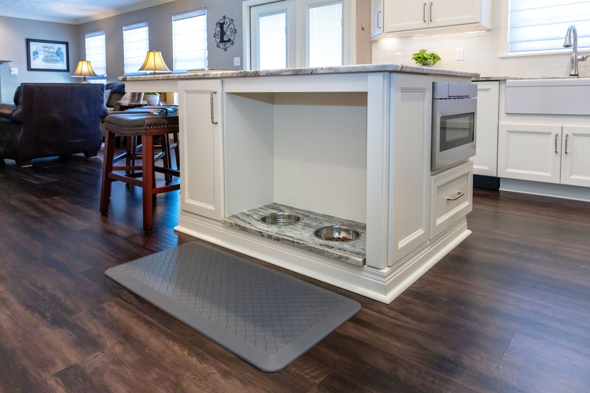 Modern kitchen with a white island, built-in oven, and dark wood floors in an open living space