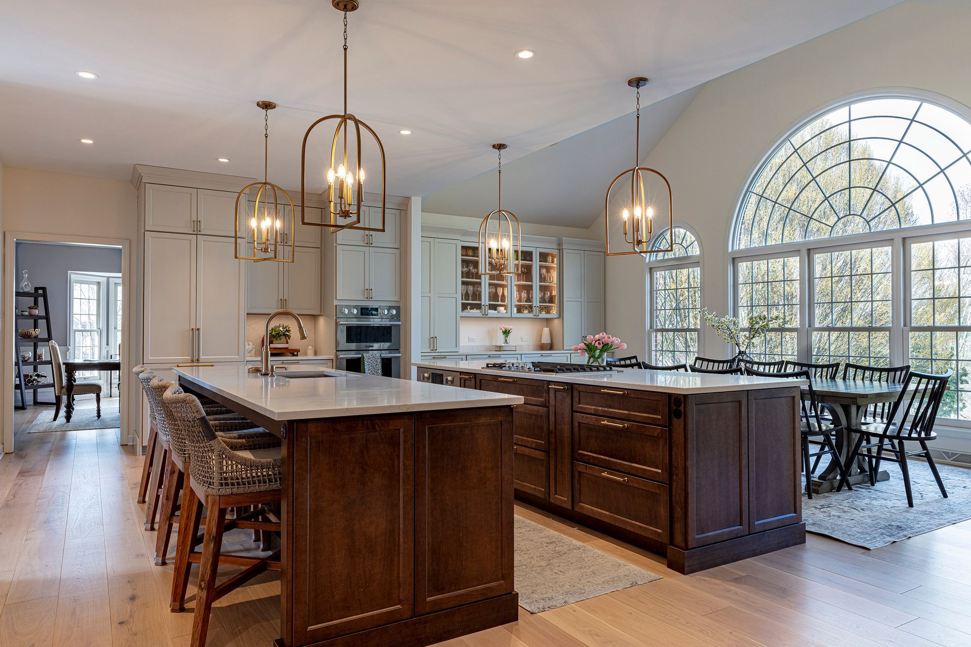 Modern kitchen with large island, wood cabinetry, pendant lights, and a bright arched window seating area