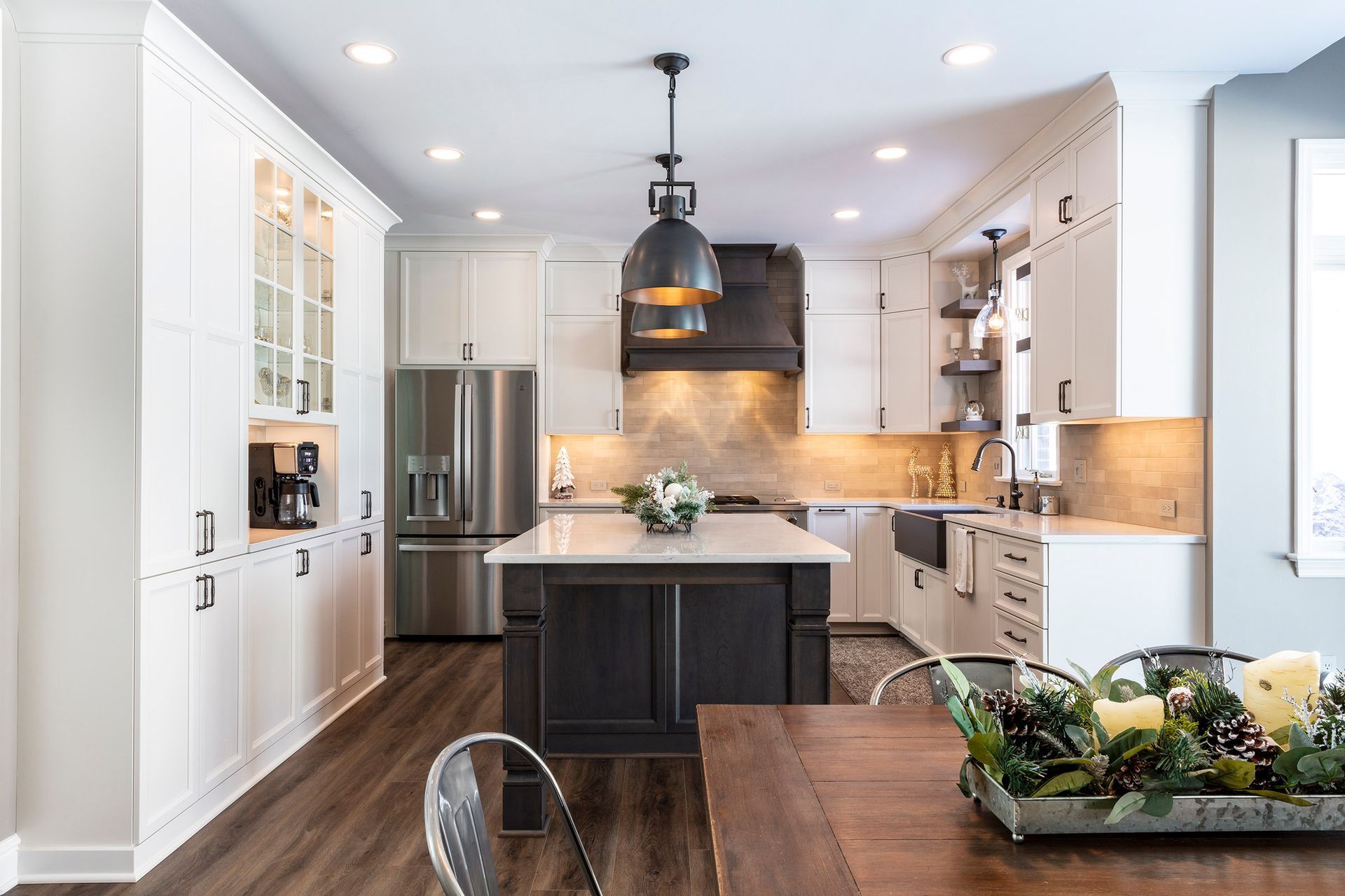 Bright modern kitchen with white cabinets, dark island, pendant light, and wood dining table