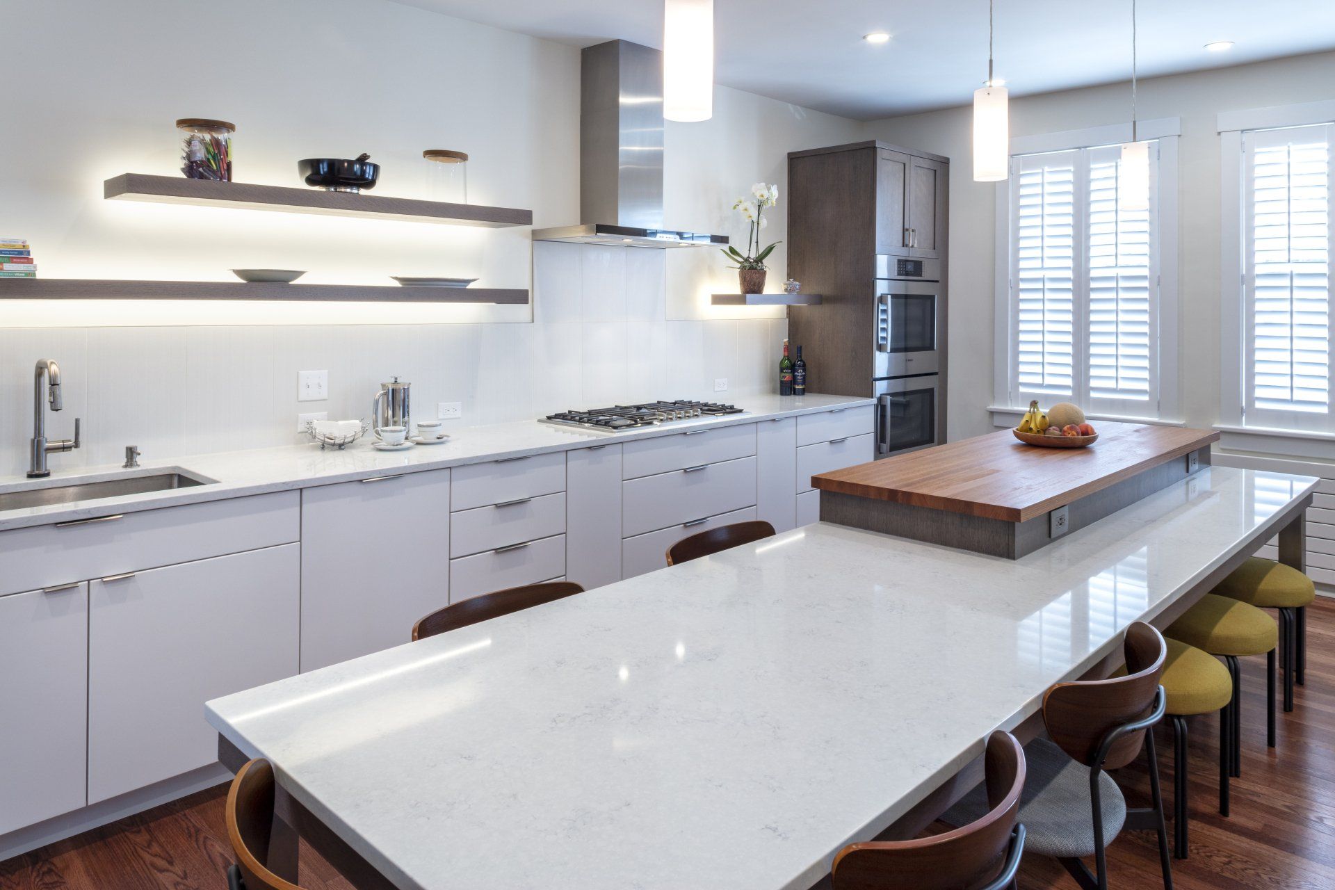 Modern white kitchen with marble island, stools, stainless appliances, and open shelving