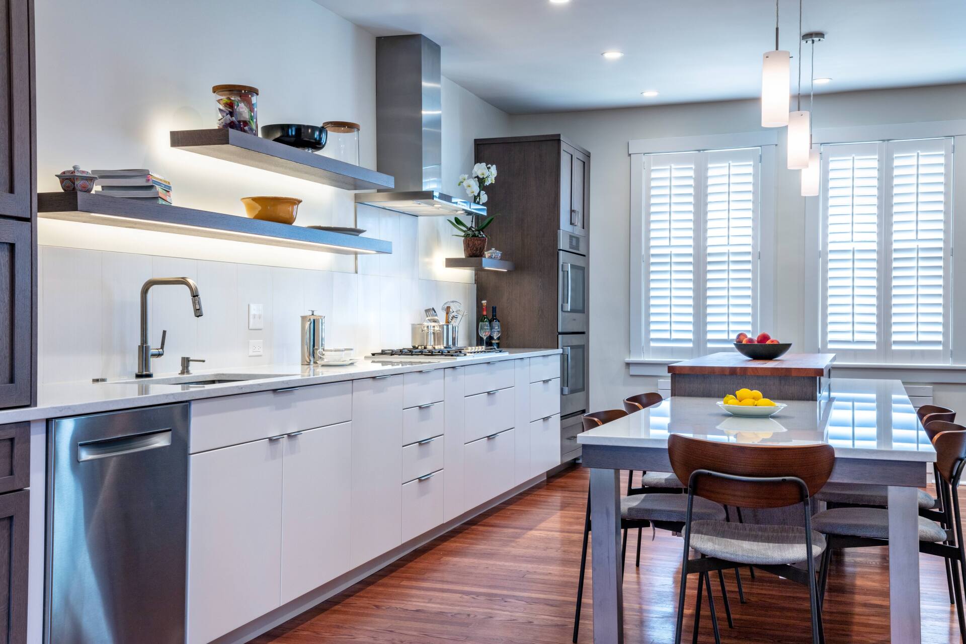Bright modern kitchen and dining area with white cabinets, wood floor, and a table by a window