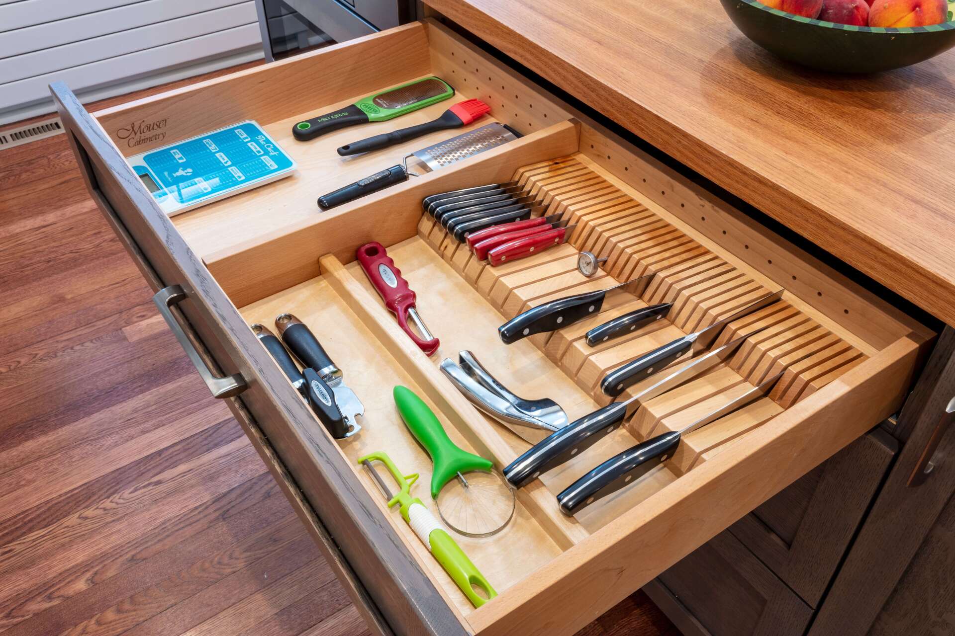 Open kitchen drawer with neatly arranged knives, kitchen tools, and utensils in a wooden organizer.