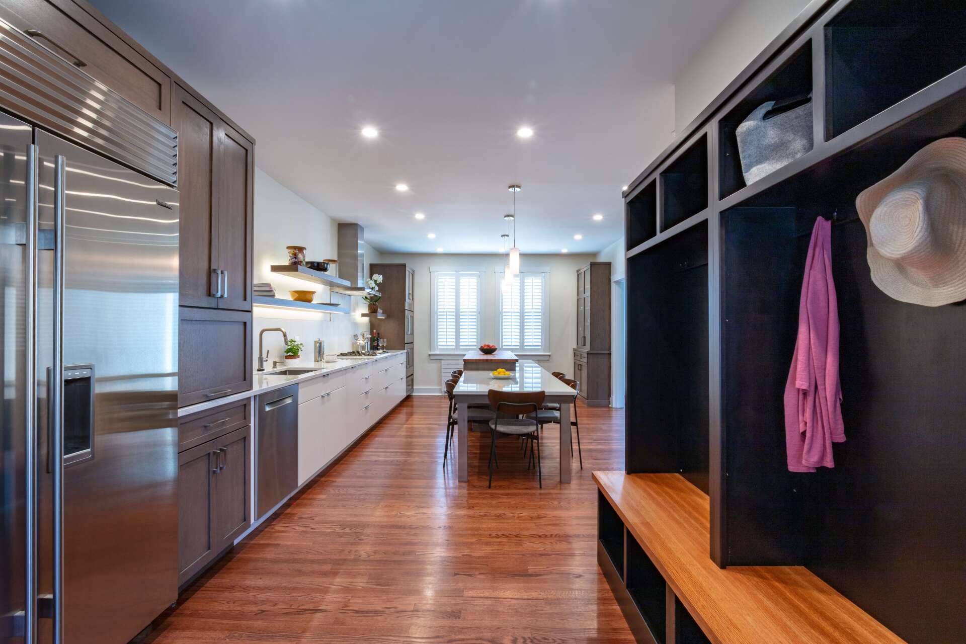 Modern kitchen with stainless appliances, wood floors, island table, and built-in coat storage