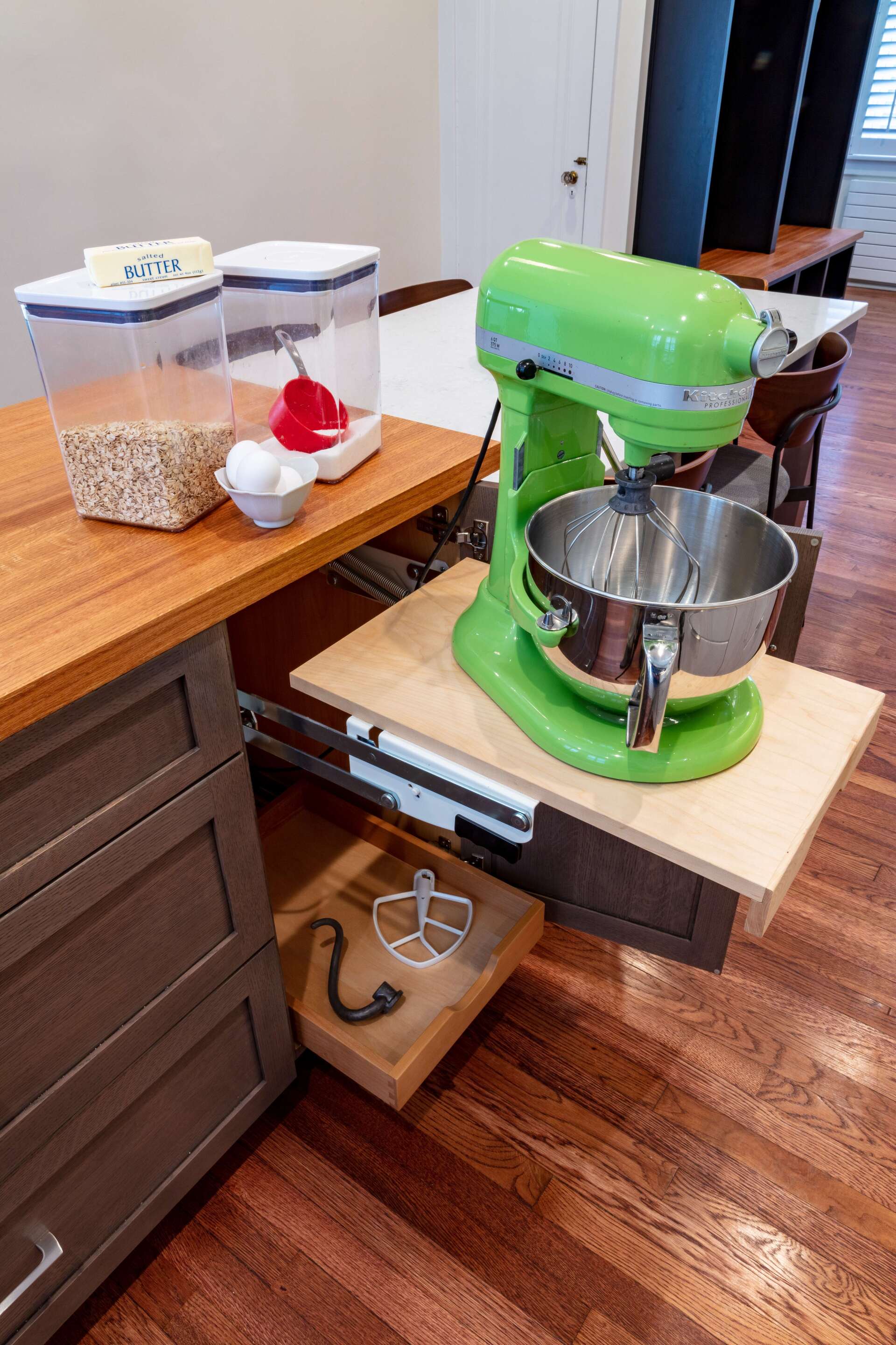 Green stand mixer on a pull-out wooden countertop in a kitchen.