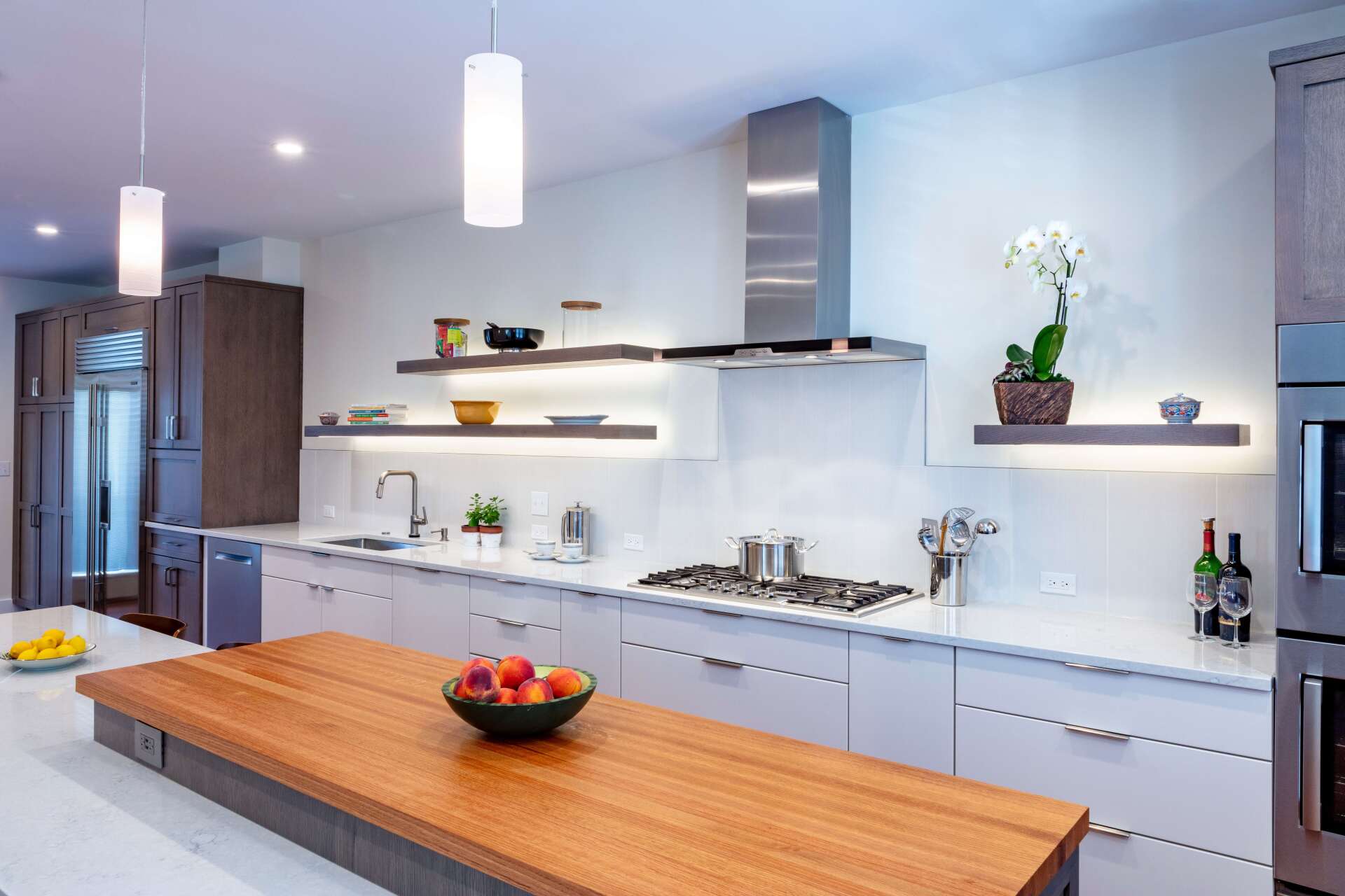 Modern white kitchen with wooden island, stainless appliances, and pendant lights