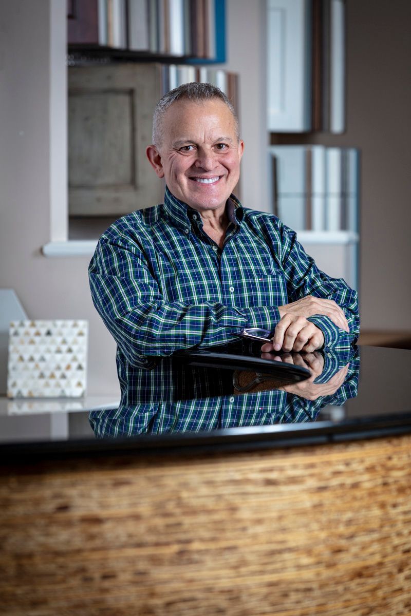 Smiling man in a blue plaid shirt leaning on a counter in a modern office lobby