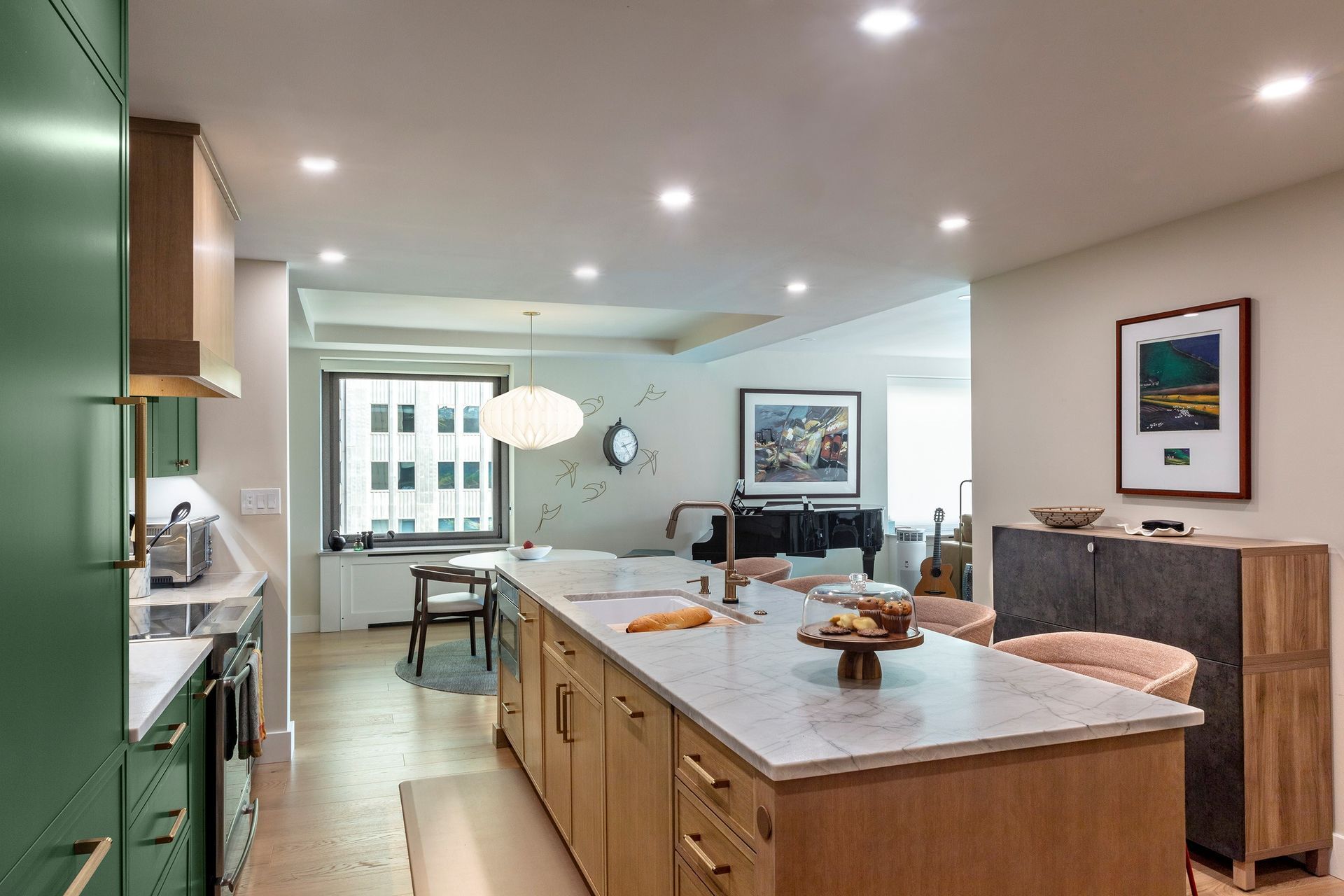 Bright, modern kitchen with island, green cabinets, bar stools, and dining area visible in the background