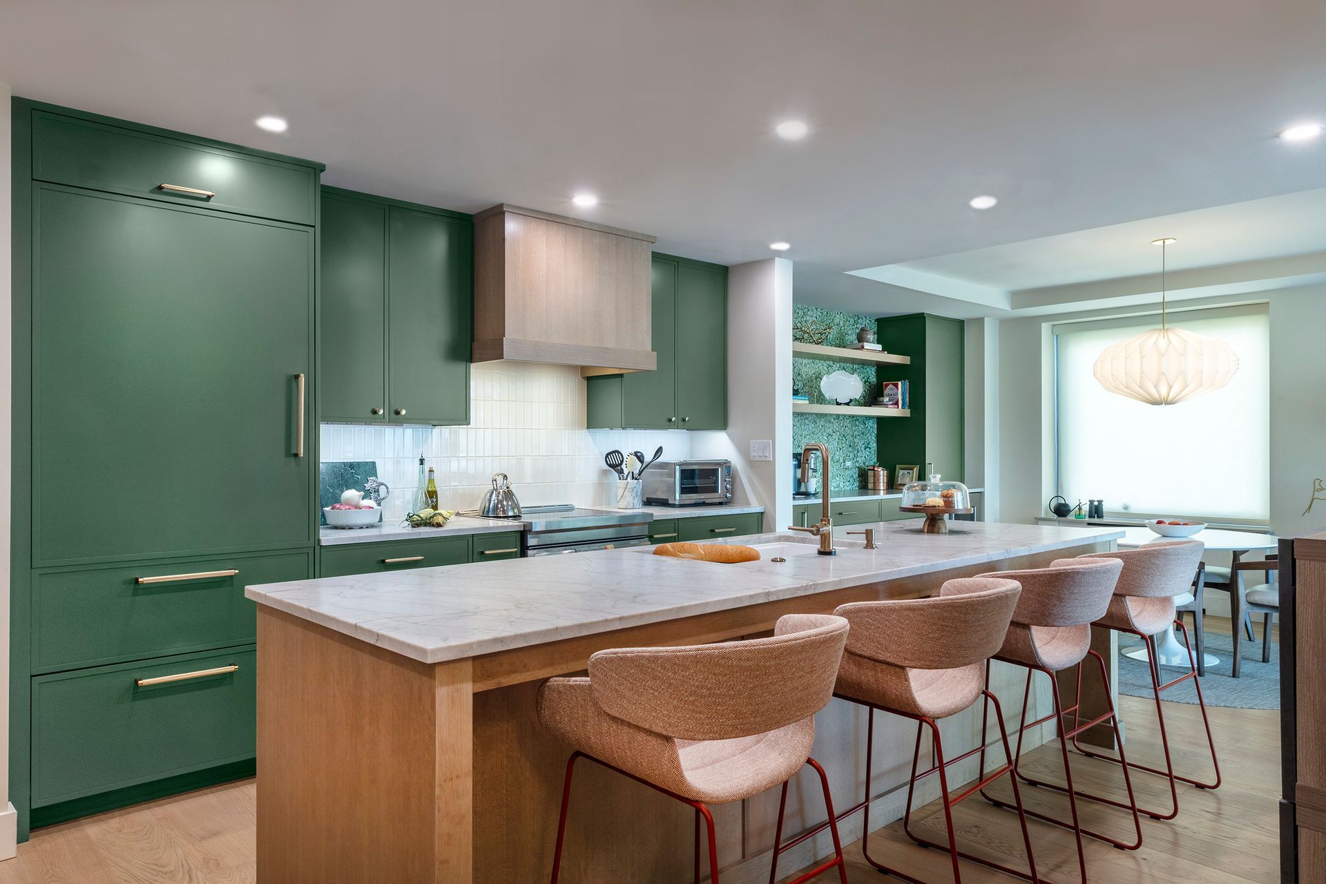 Modern kitchen with green cabinets, a long island, and four bar stools under recessed lighting