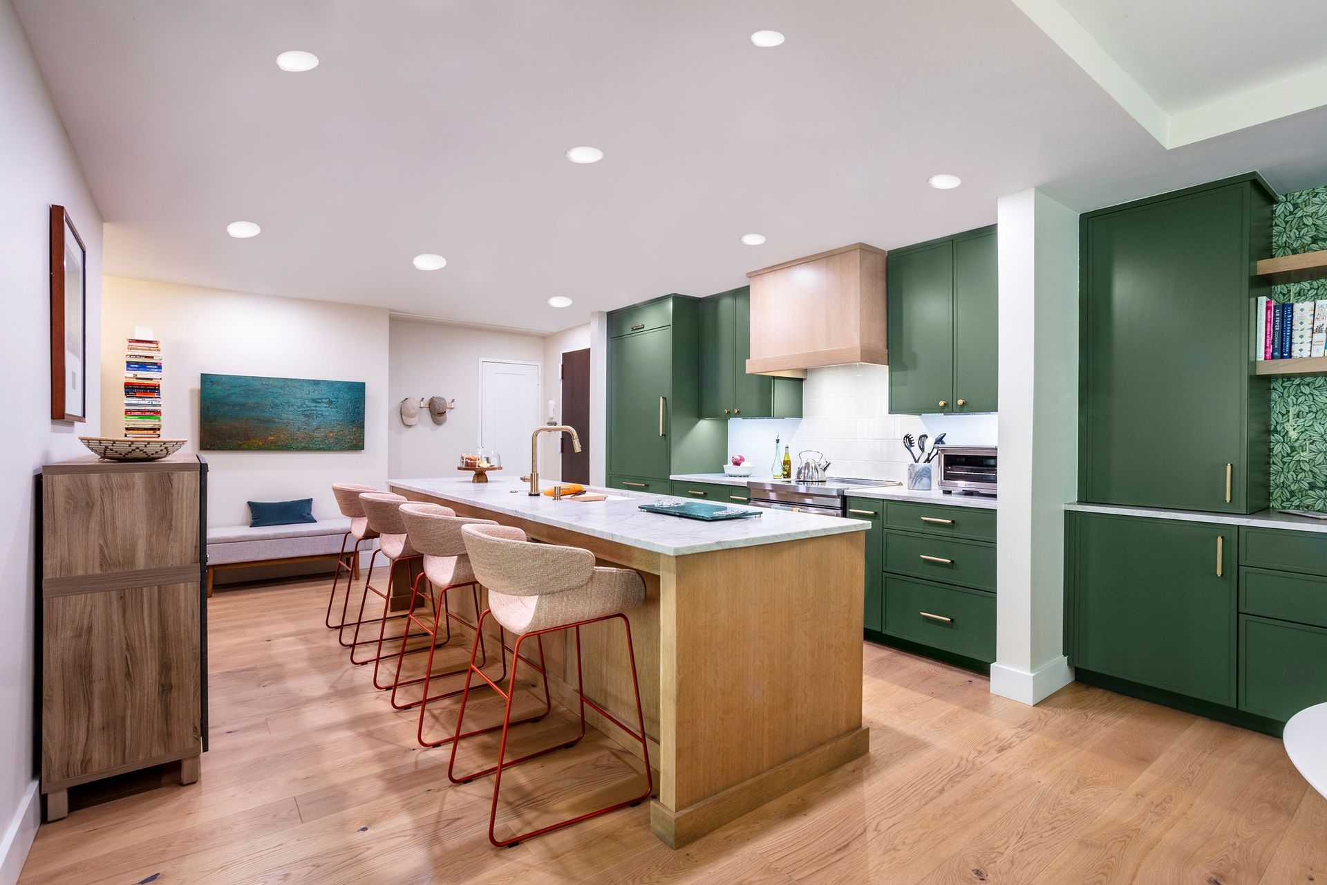 Modern kitchen with green cabinets, white island, and copper stools in a bright open-plan home