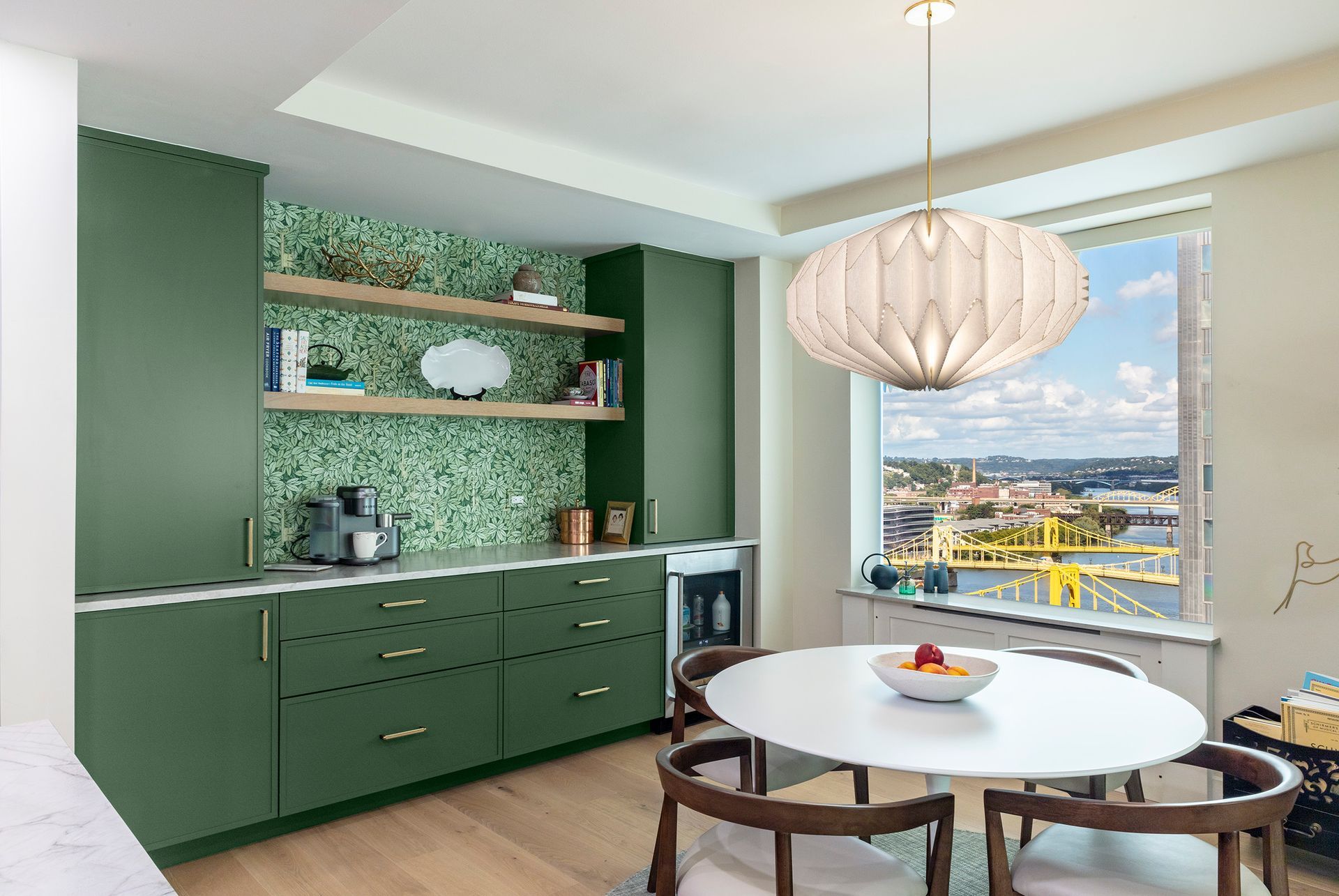Modern green kitchen and dining nook with round table, pendant light, and large window view