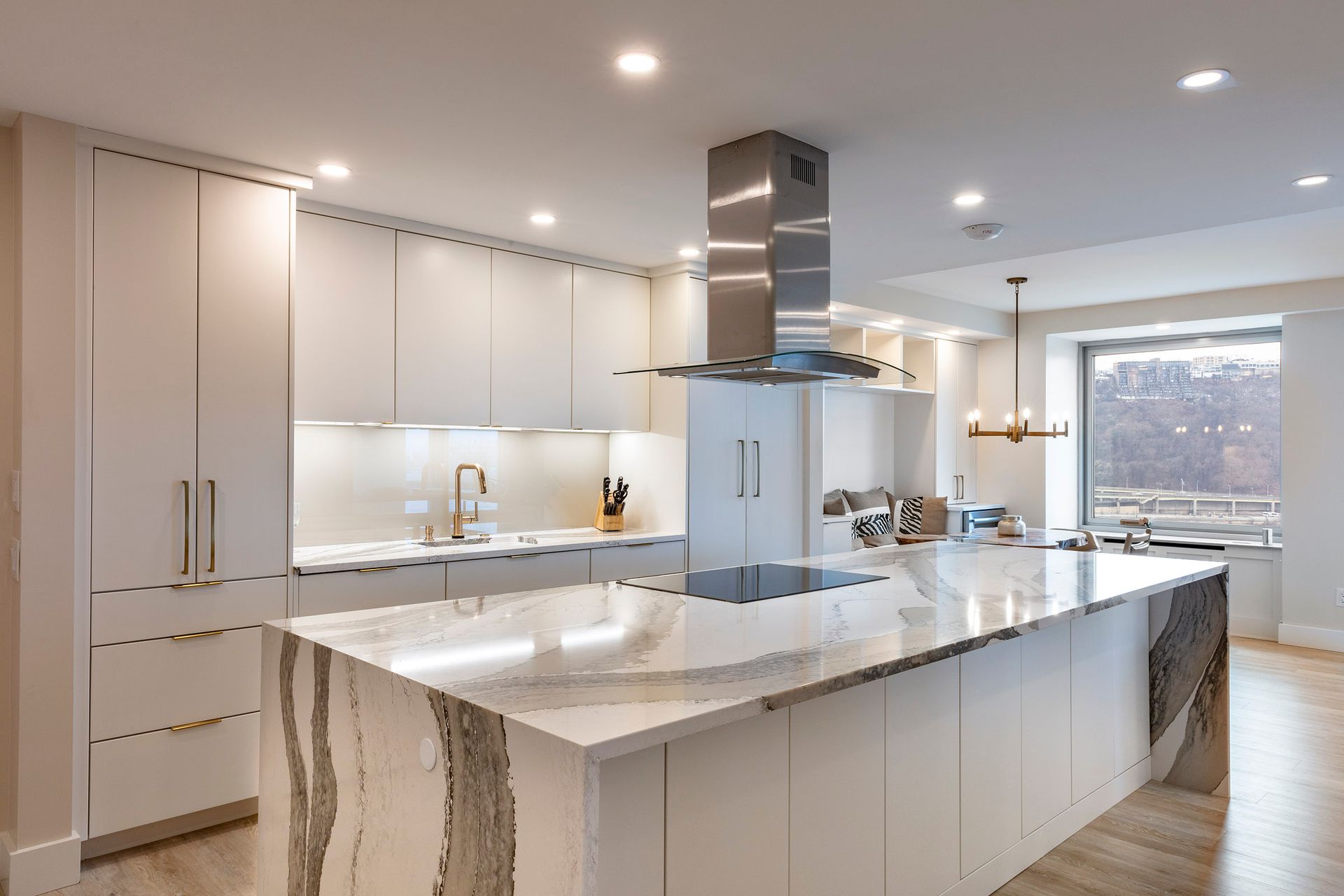 Bright modern white kitchen with large island, marble countertops, and stainless steel range hood.