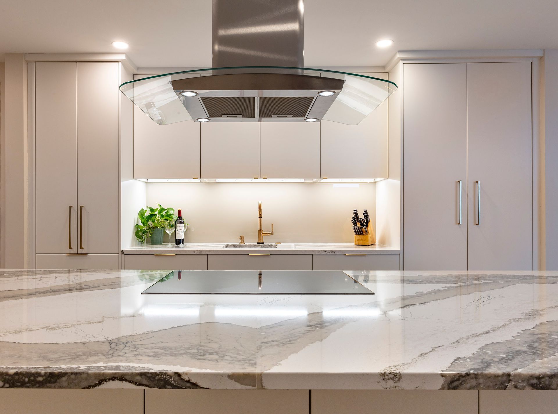 Modern white kitchen with marble island, gold hardware, and stainless steel range hood