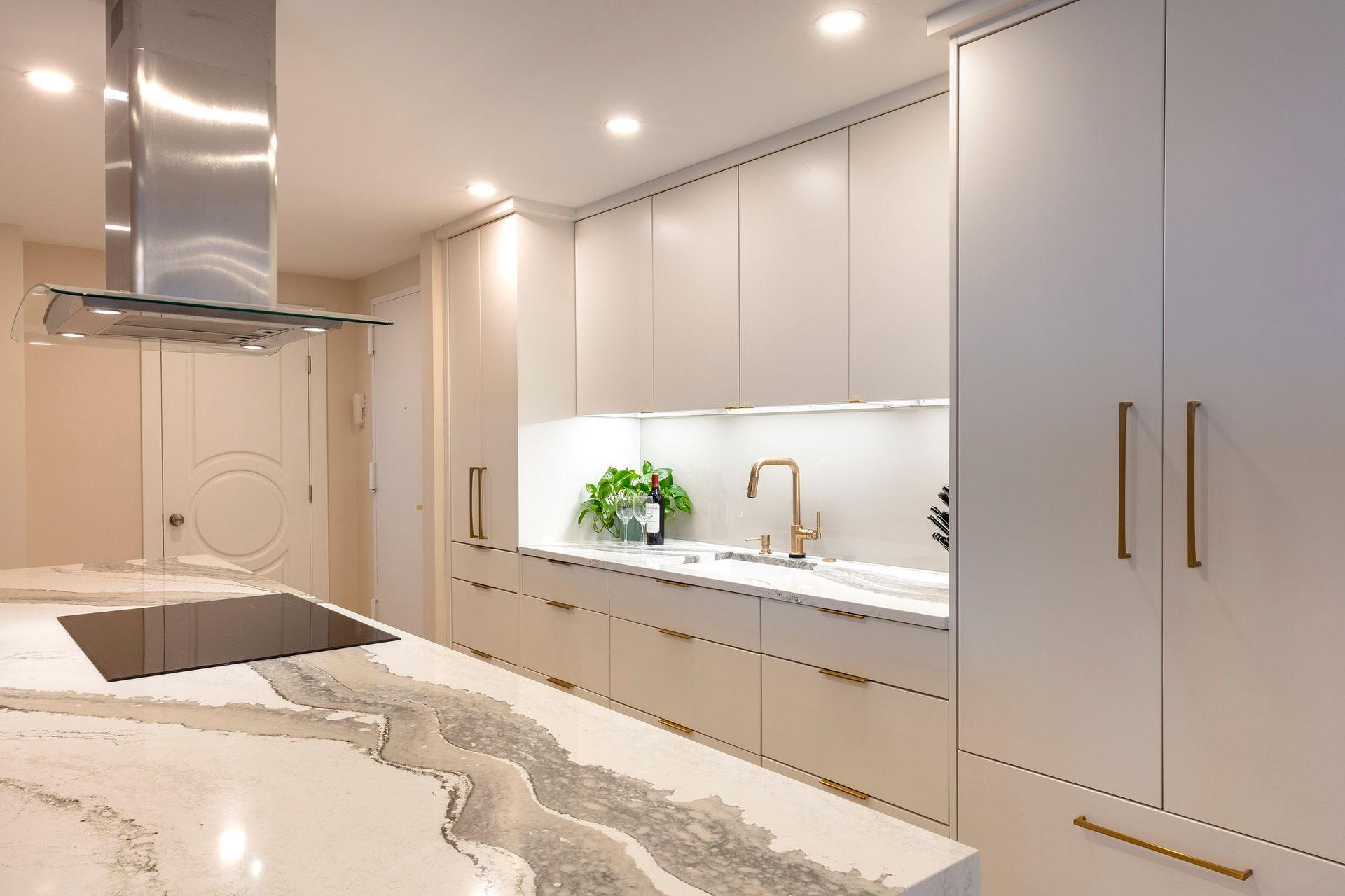 Modern white kitchen with marble island, built-in cabinets, and stainless steel range hood