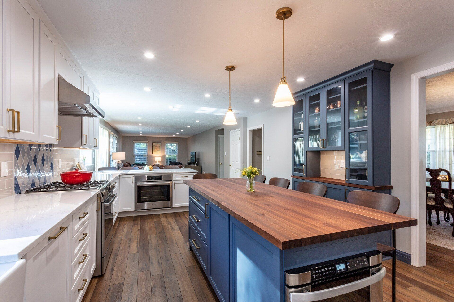 Modern kitchen with large blue island, white cabinets, pendant lights, and wood floors