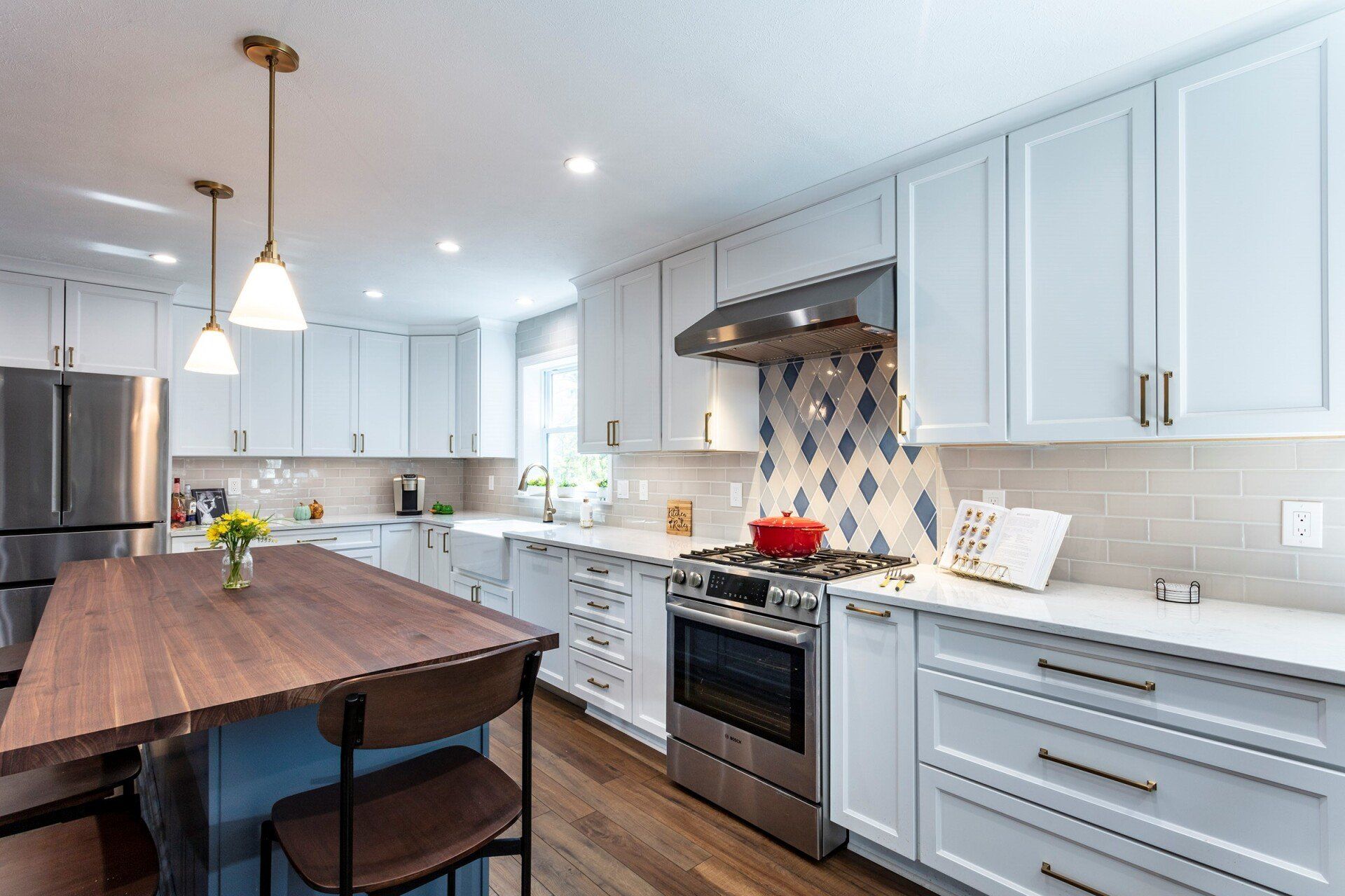 Bright modern kitchen with white cabinets, stainless oven, wood island table, and pendant lights
