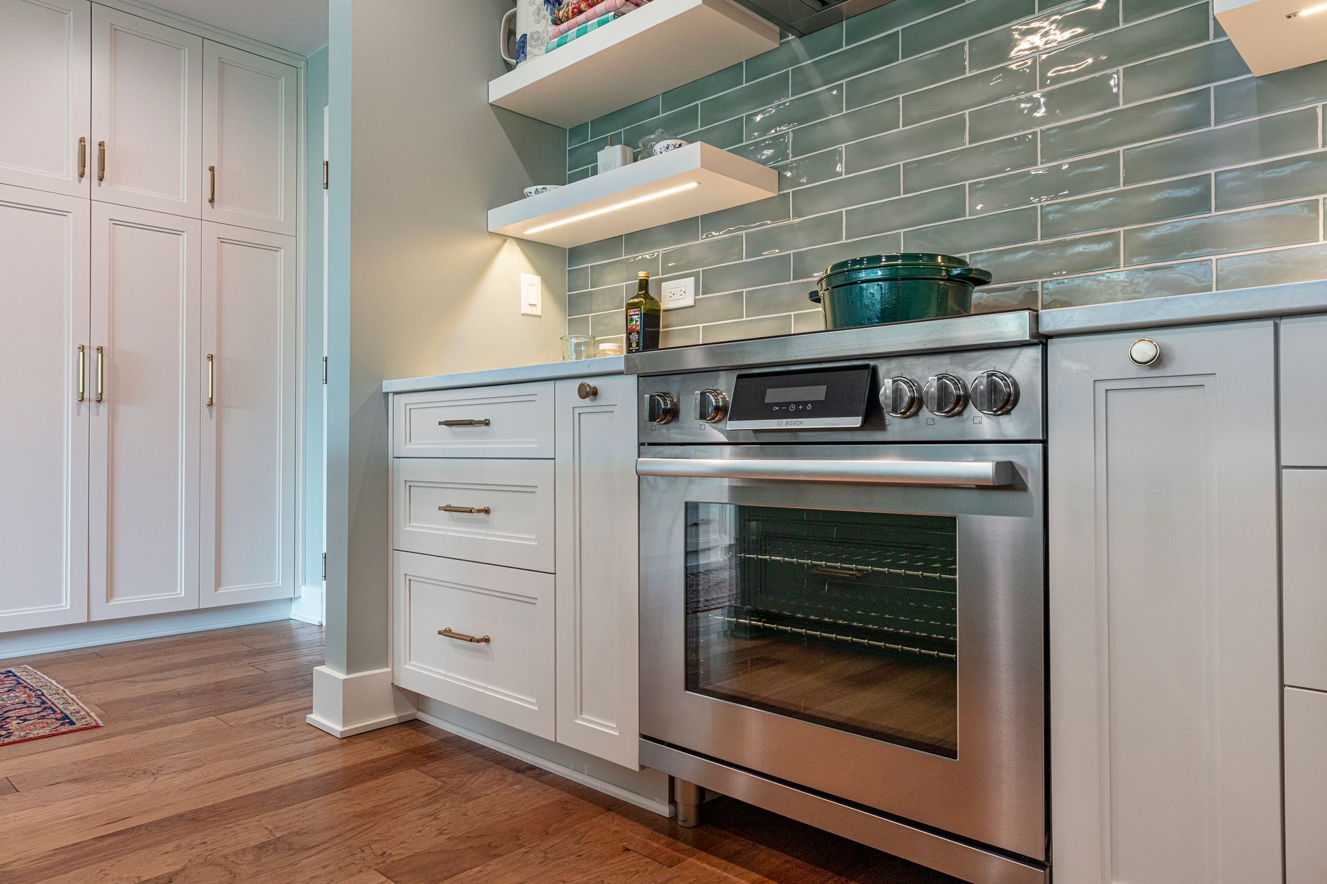 Modern kitchen with white cabinets, stainless steel stove, and pale blue tile backsplash