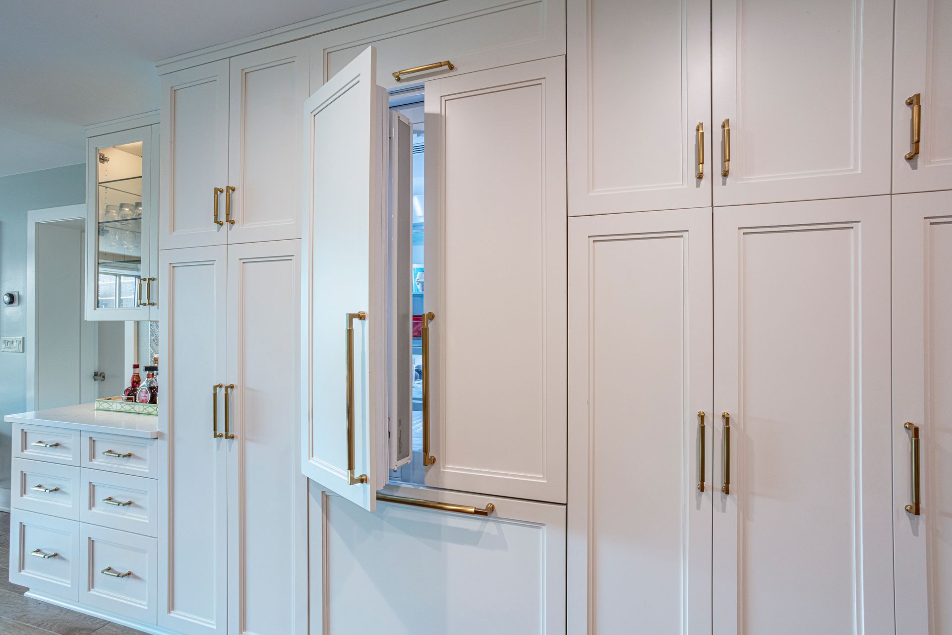 White built-in cabinets with a small open window and a vanity reflected in a mirror on the left.
