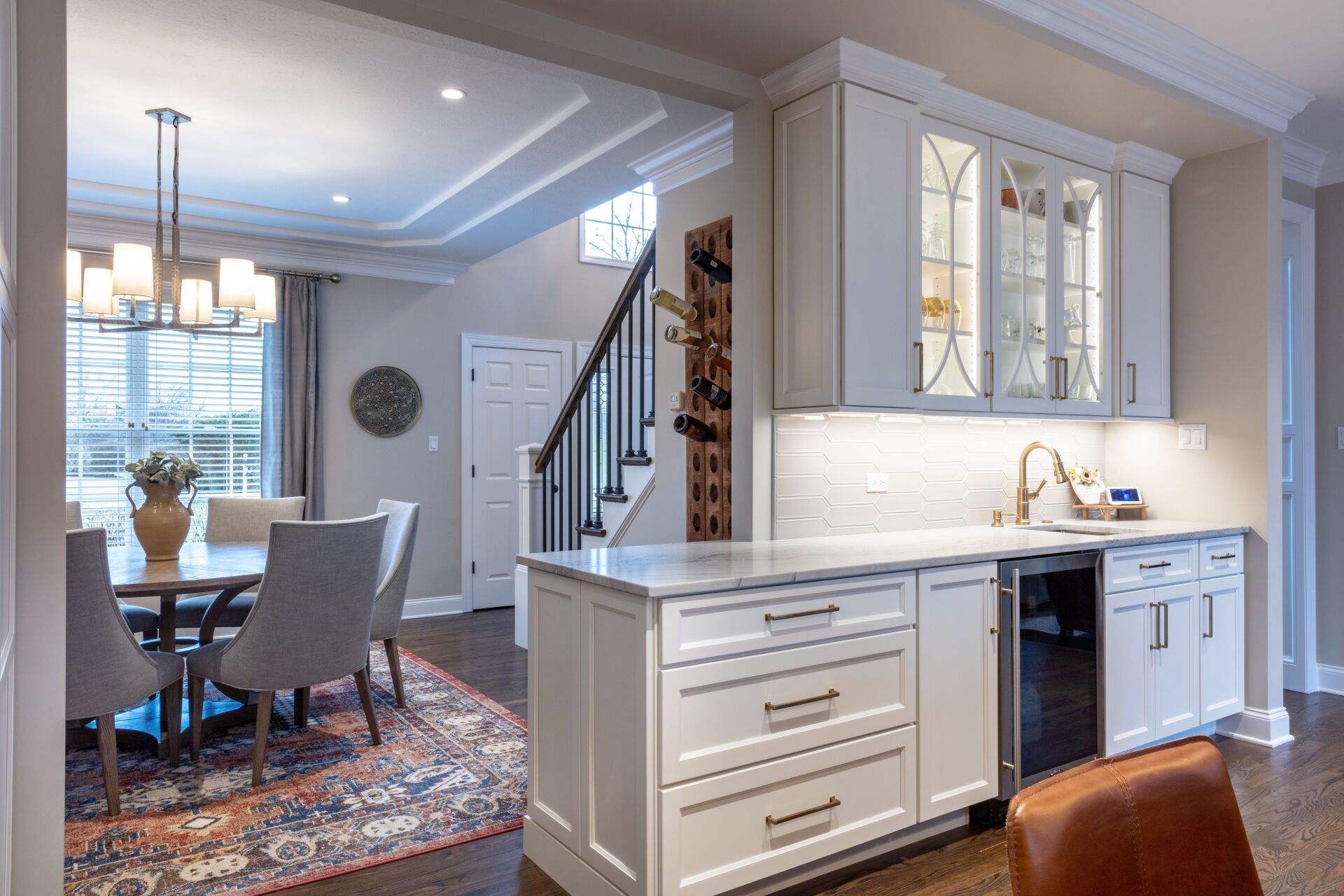 Bright modern kitchen and dining area with white cabinets, island, and patterned rug, viewed from the hallway