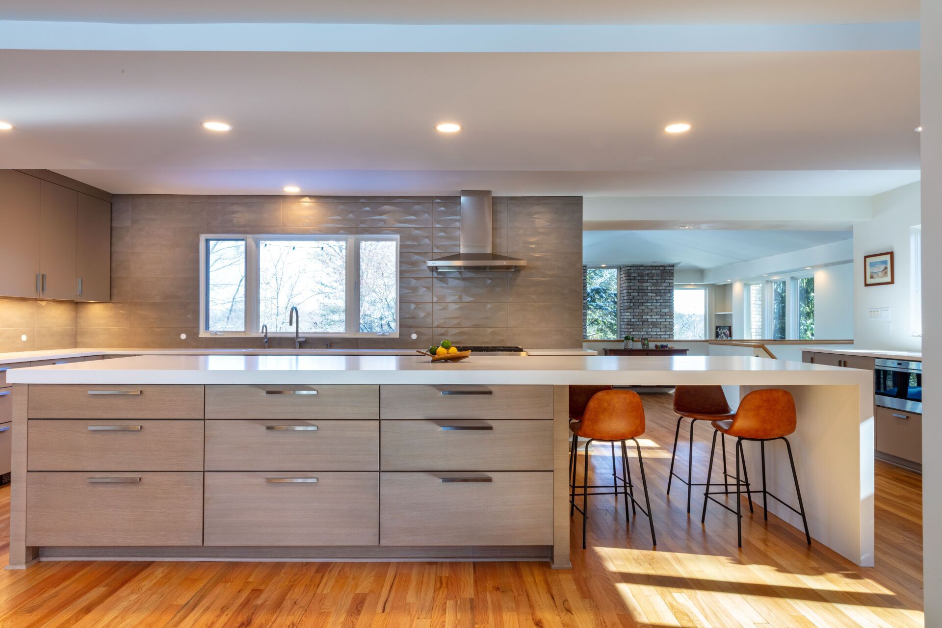 Modern kitchen with light wood cabinets, white island, and orange bar stools under a window