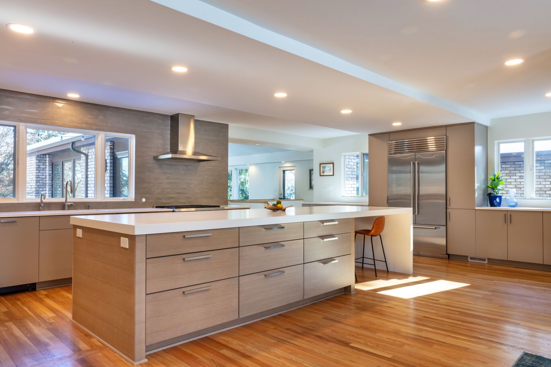 Bright modern kitchen with large island, white countertops, wood floors, and stainless steel appliances