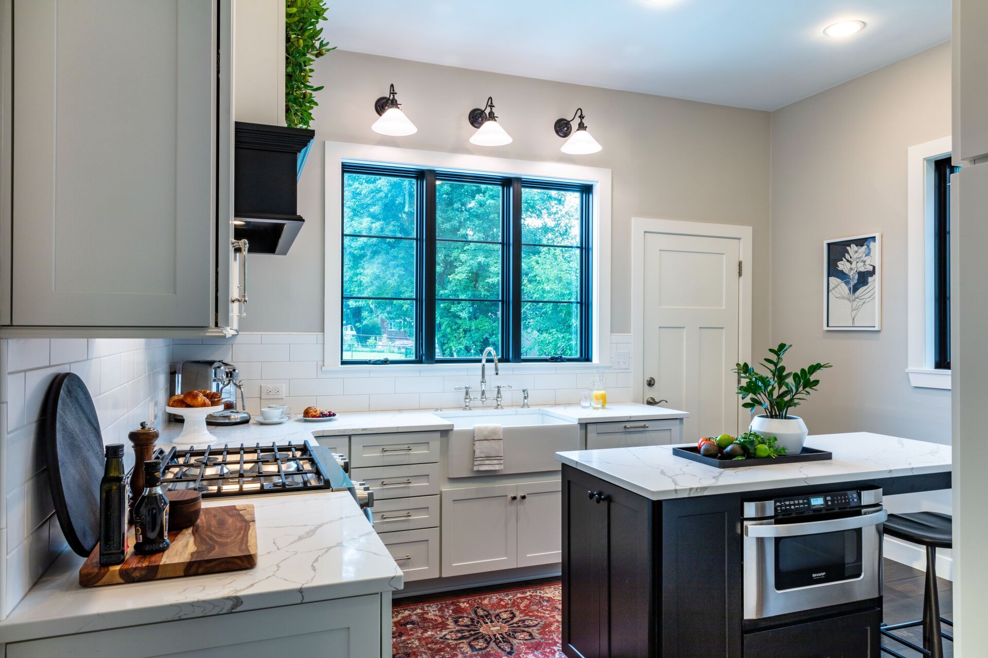 Bright modern kitchen with white cabinets, black island, window over sink, and pendant lights