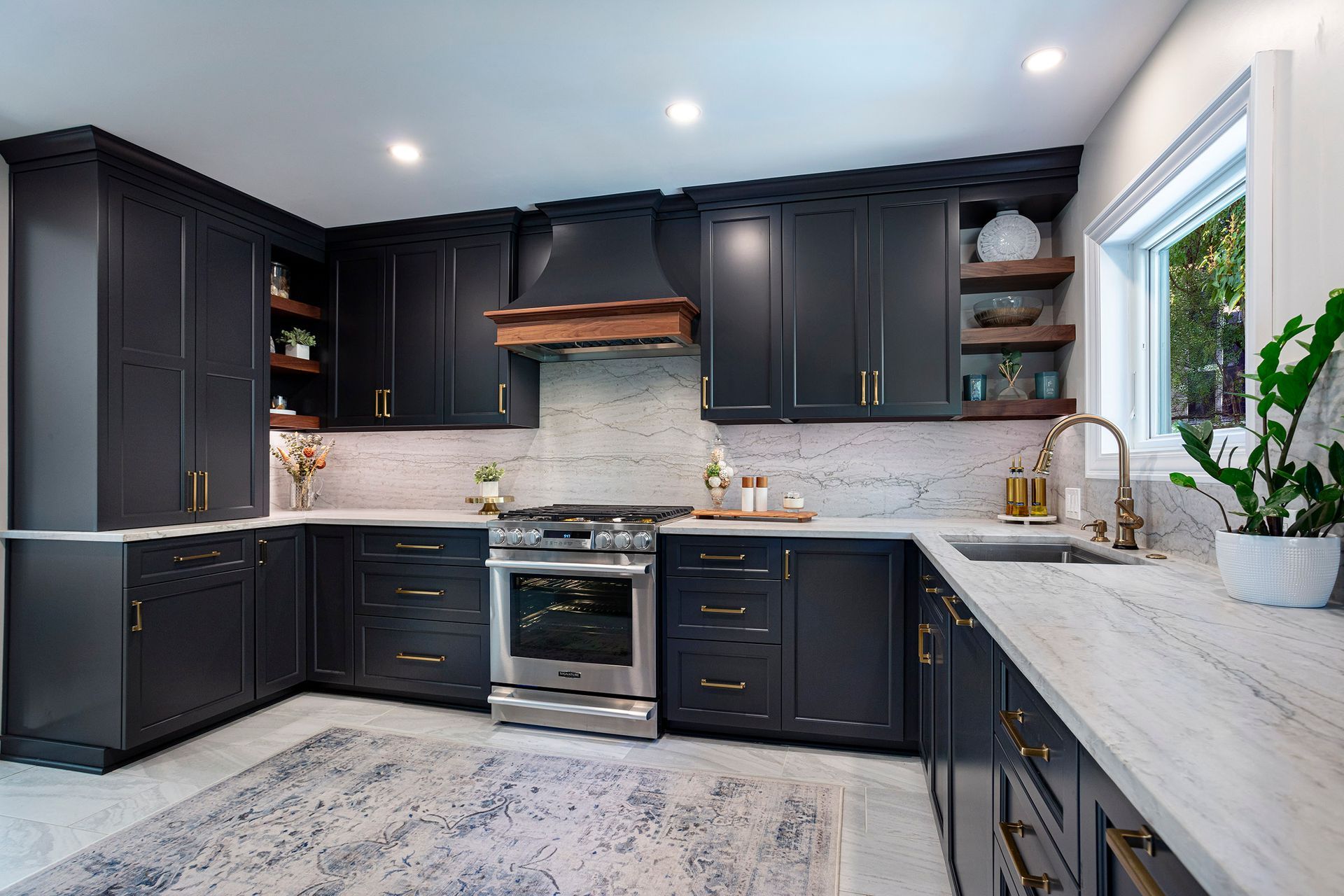 Modern dark kitchen with black cabinets, marble counters, stainless stove, and white tile backsplash
