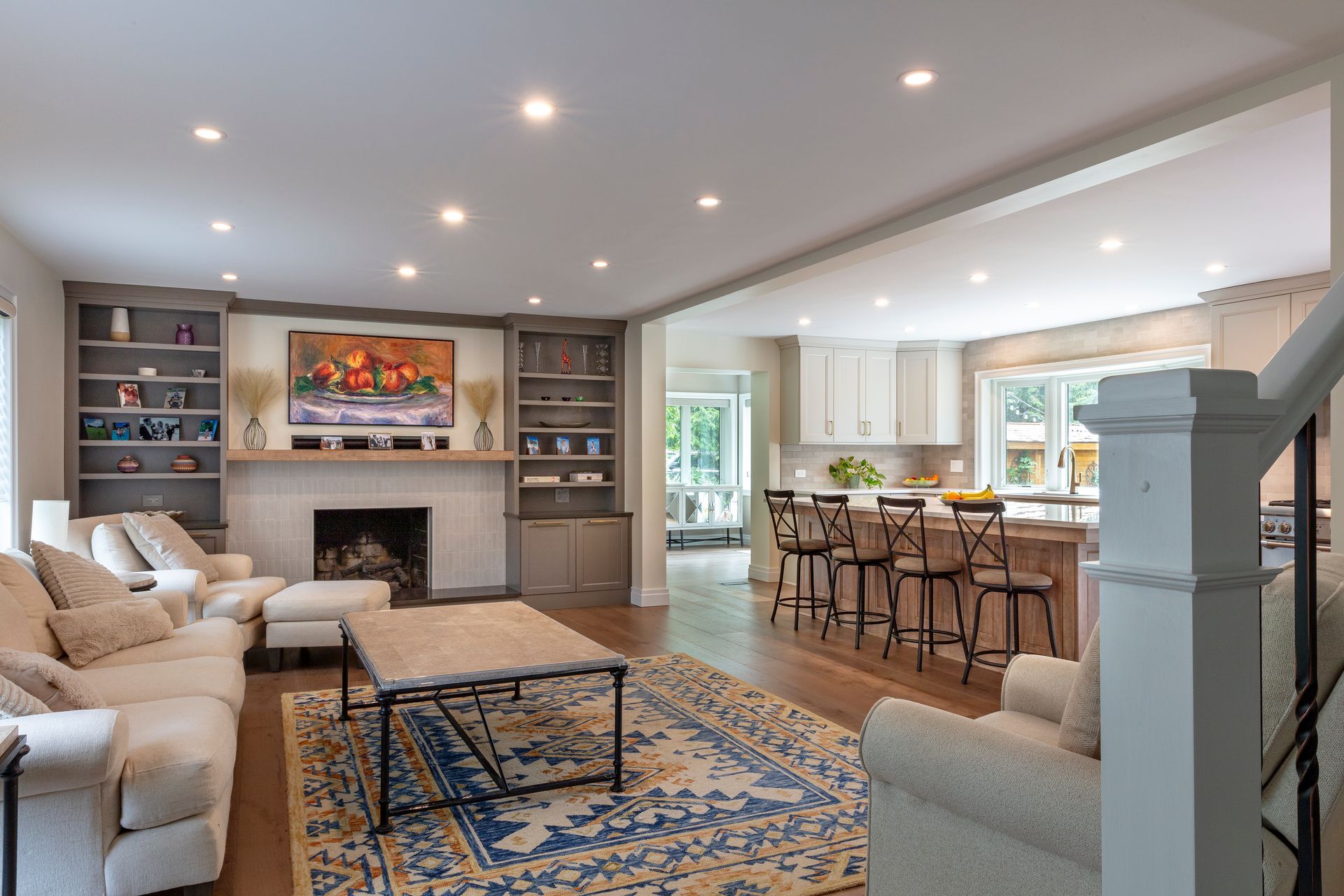 Bright open living room with fireplace, built-in shelves, beige sofas, and a kitchen island in the background