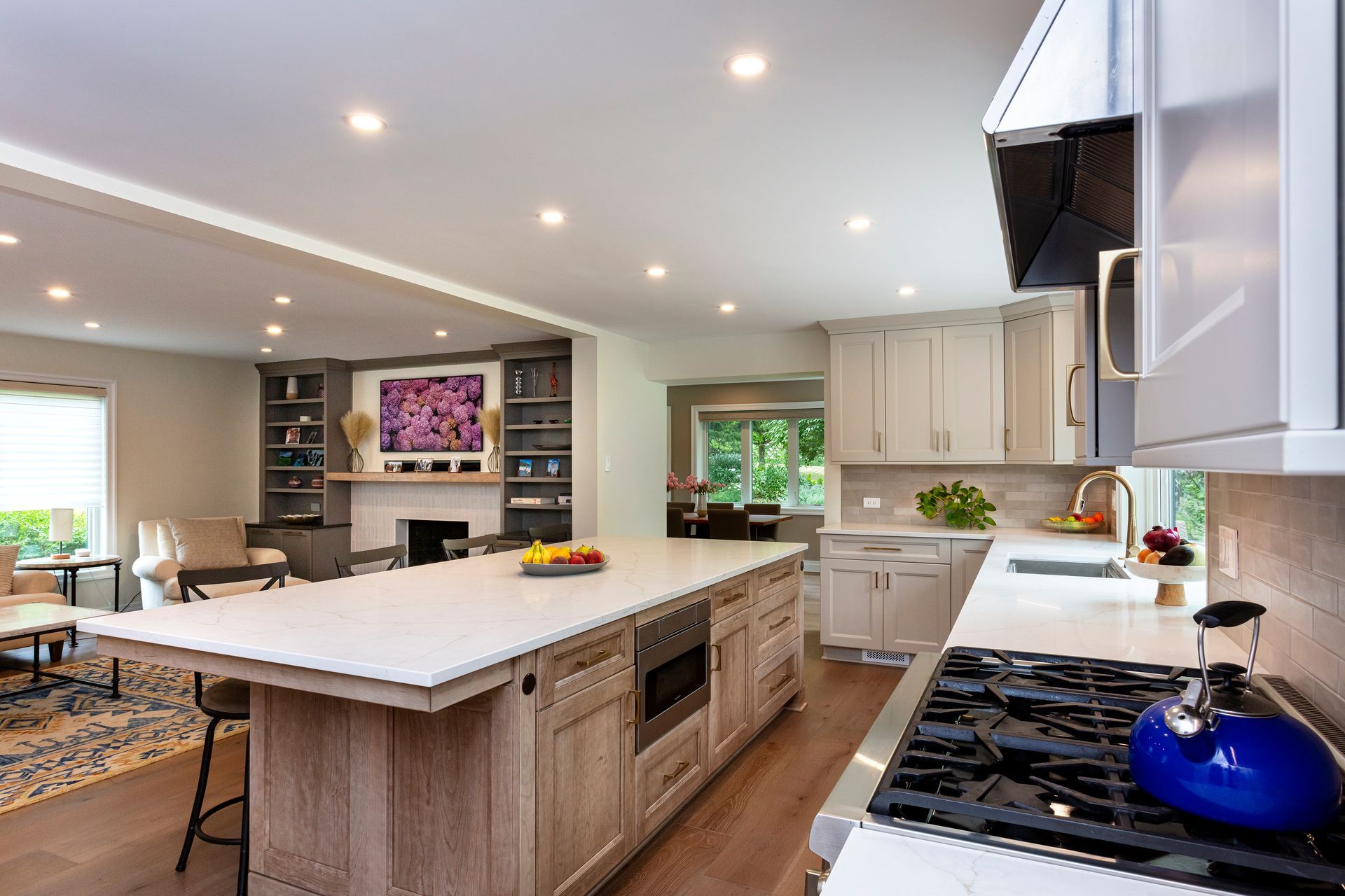 Bright modern kitchen with large island, white cabinets, stainless appliances, and blue pot on the stove.