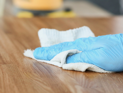 Blue-gloved hand wiping a wooden surface with a white cloth