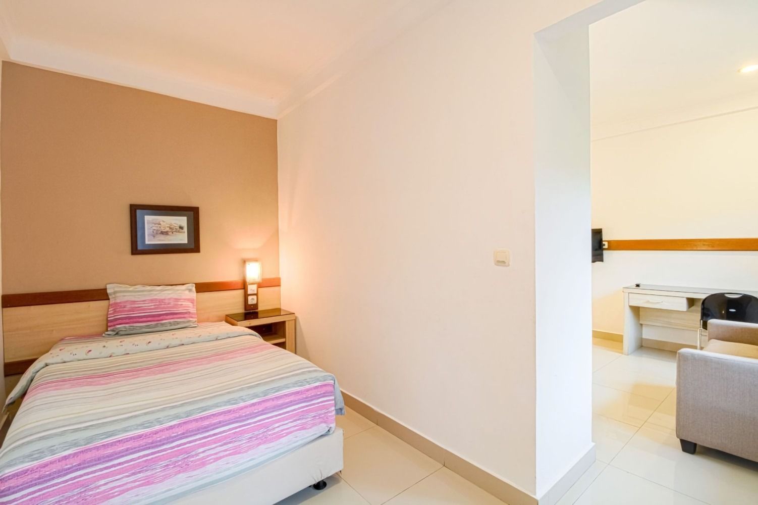Bedroom with a single bed, nightstand, and doorway to another room with furniture.