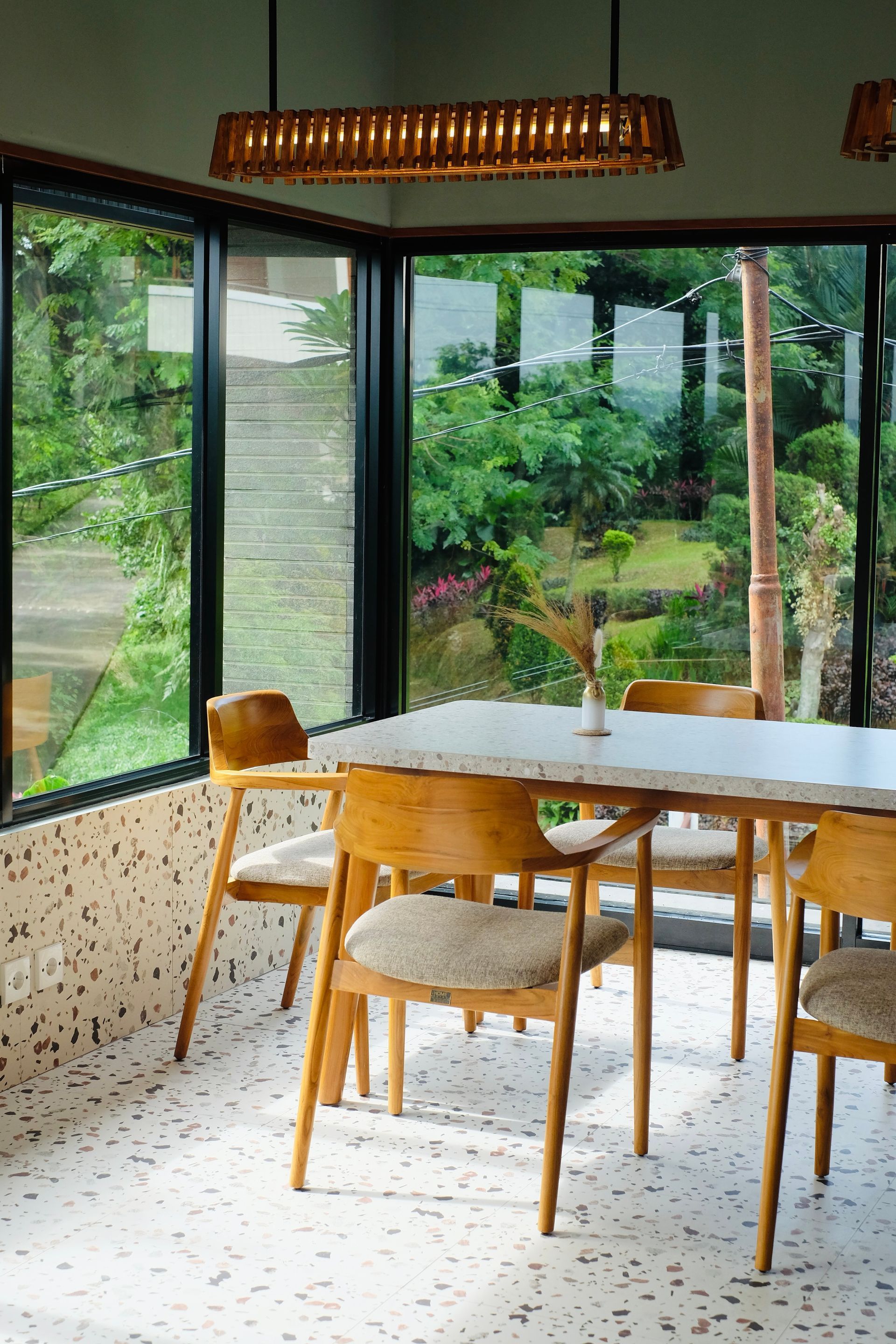 Cafe interior with wood table, chairs, and large windows overlooking a garden.