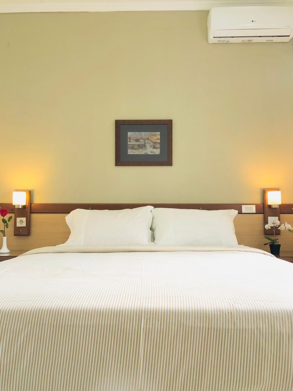 Bedroom with white bedding, headboard with lamps, picture on wall, and AC unit.