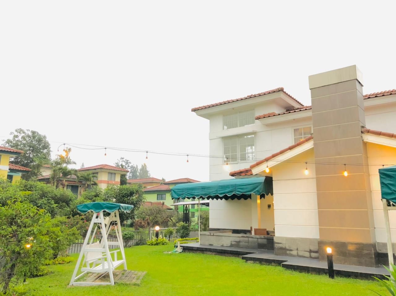 White house with a chimney and green awnings, set in a yard with a swing and other homes in the background.