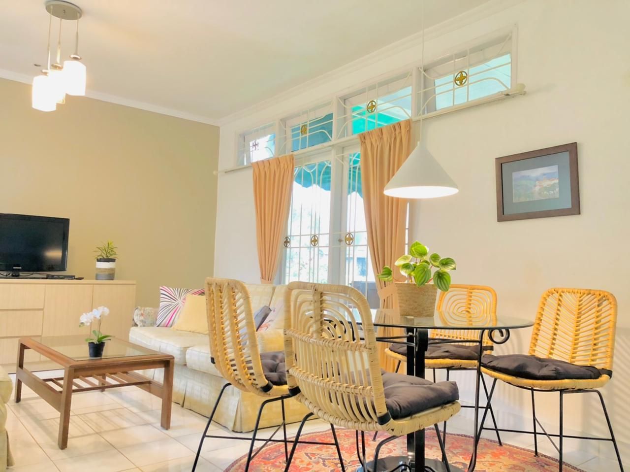 Living room with a small dining area; cream walls, rattan chairs, round table, and a neutral sofa.