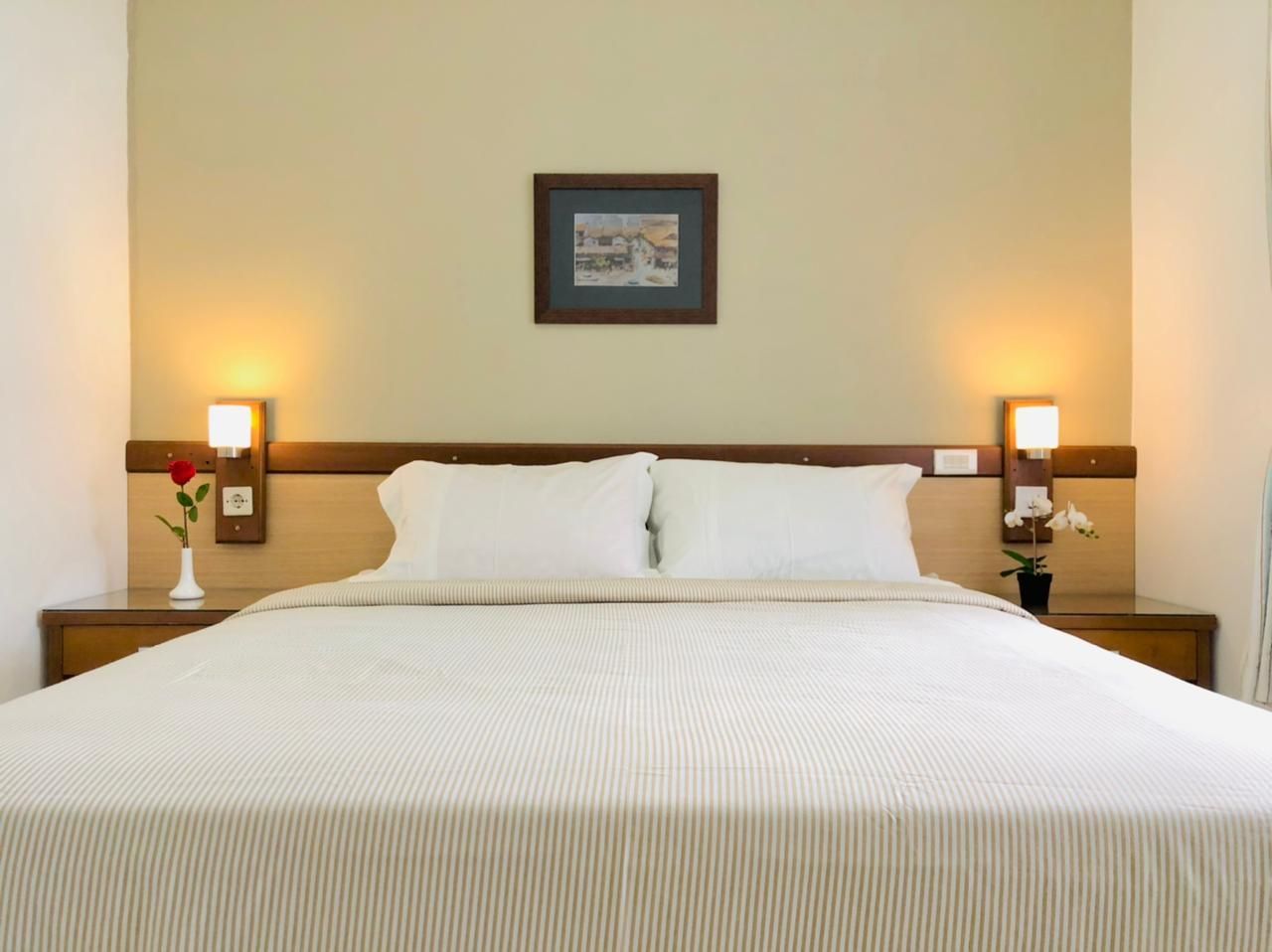 Bedroom with a made bed, nightstands, lamps, and a small framed picture above the bed.