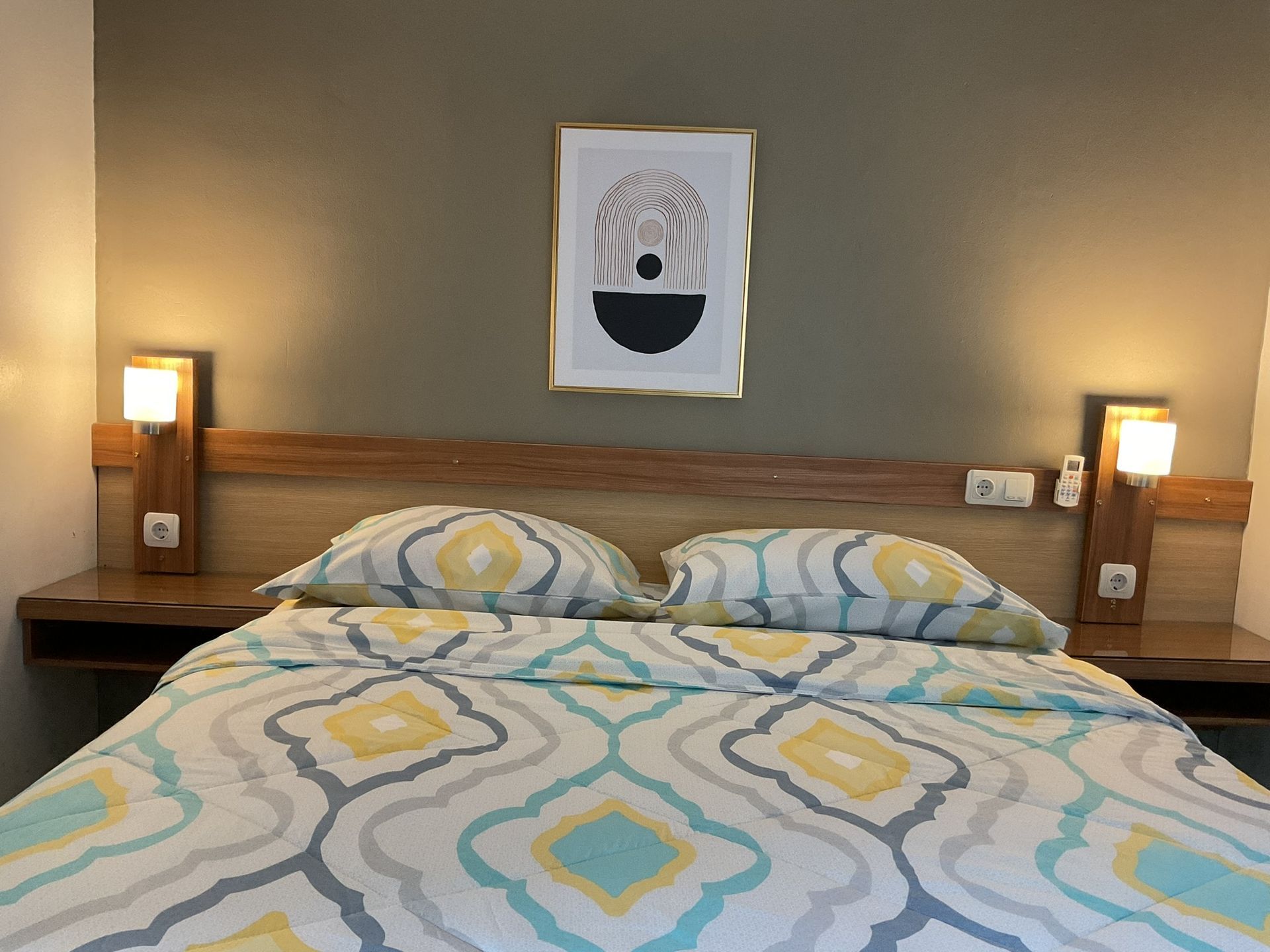 Bedroom with bed, patterned bedding, and wall art above headboard; sconces on either side.