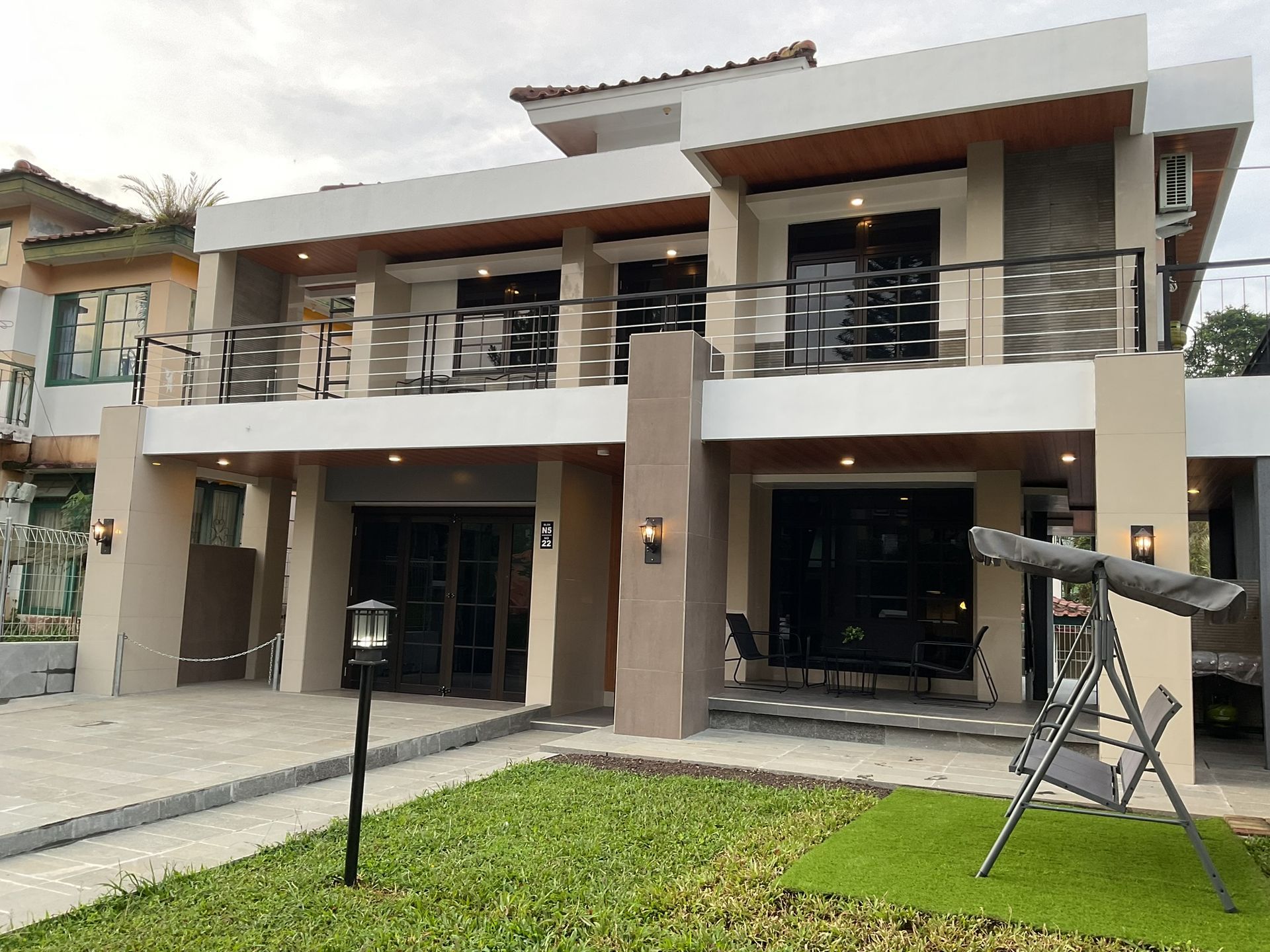 Two-story modern home with balconies, tan and white exterior, lawn in front.