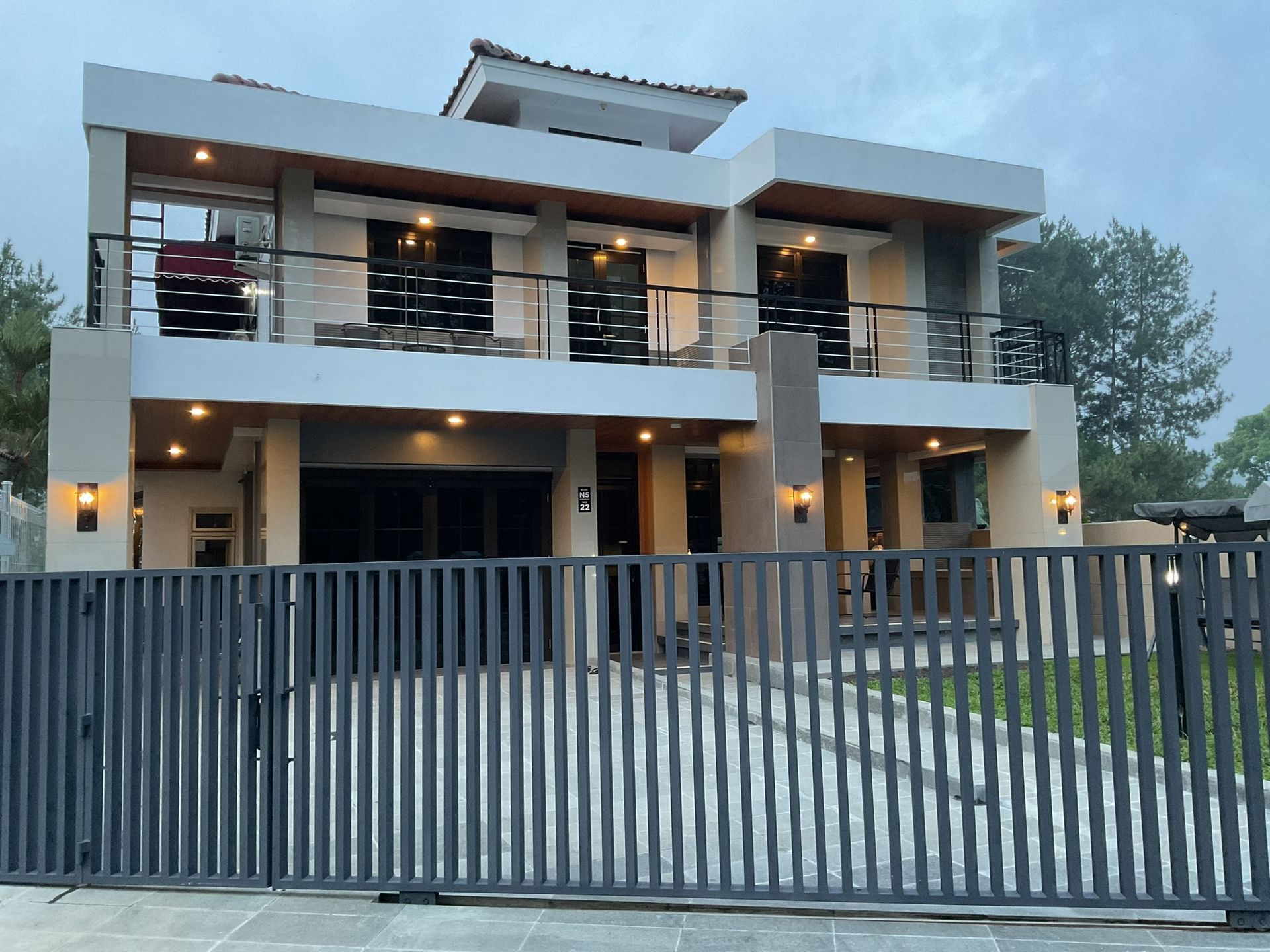 Two-story modern house with balcony, gray fence, and cloudy sky.