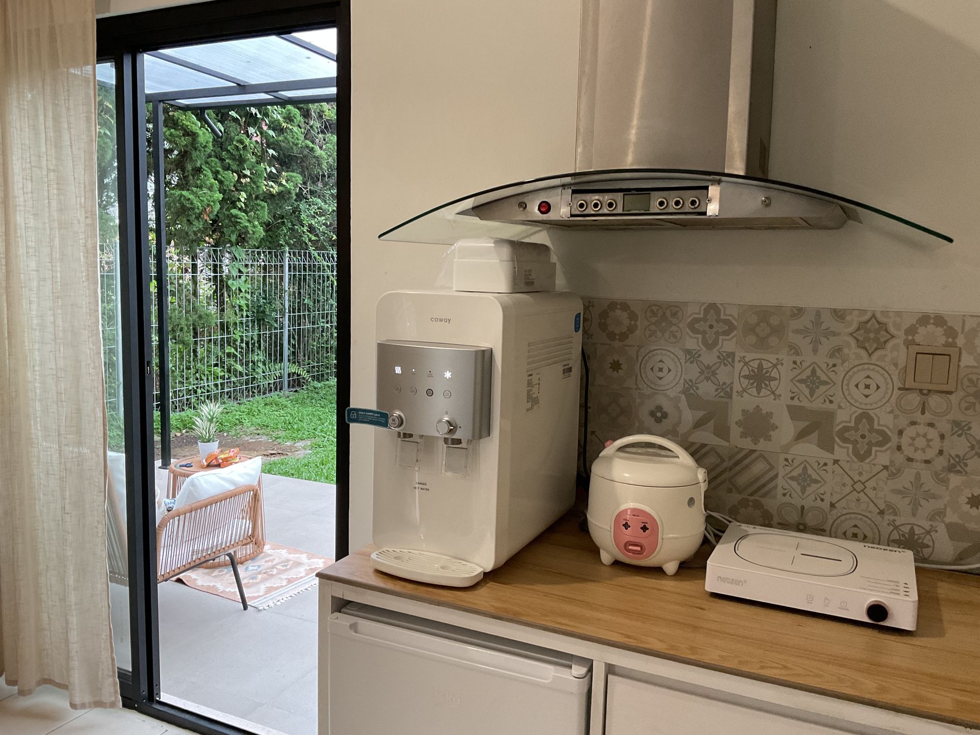 Kitchen corner: white water dispenser, rice cooker, and portable stove on countertop next to a sliding glass door.