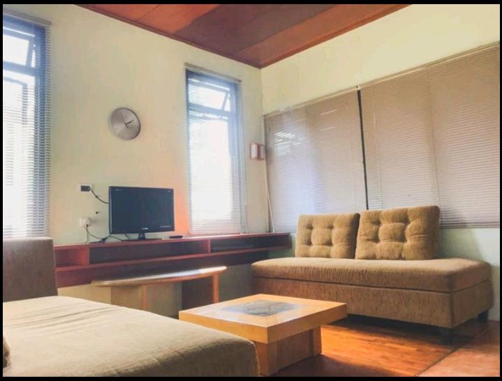 Living room with a sofa, coffee table, and TV; natural light through windows.